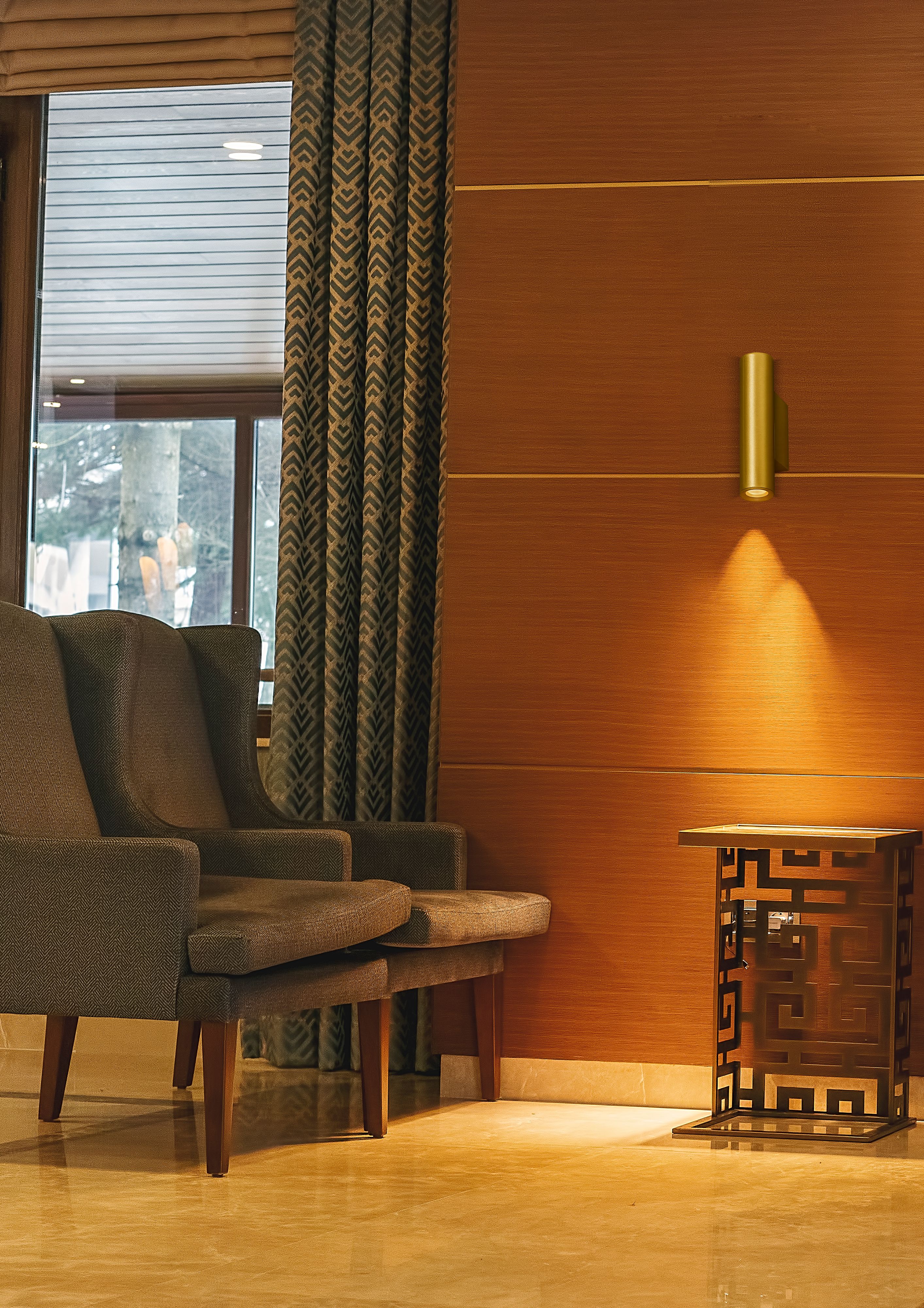 Beacon 2 Light Up/Down Wall Light in brushed gold installed on a wood panelled wall in a hotel lounge, glowing with warm downward light