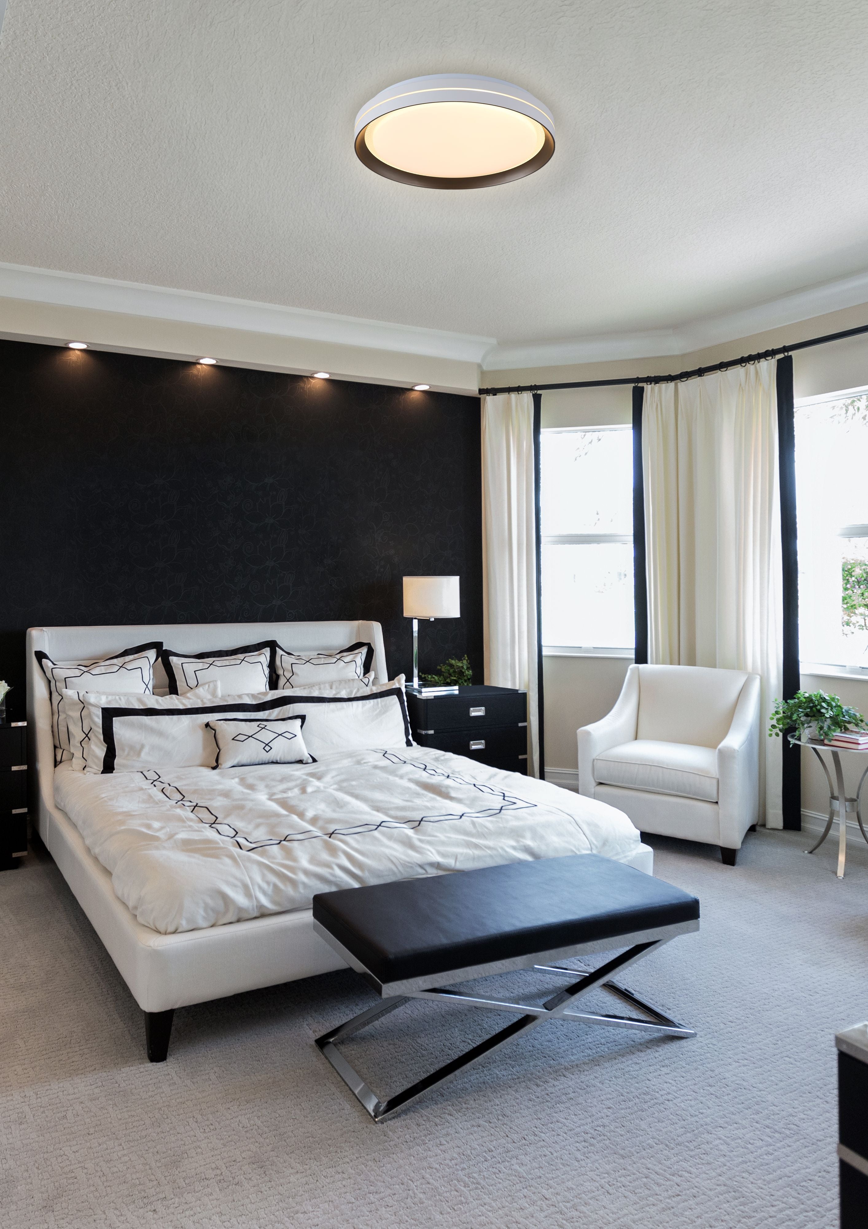 Searchlight Saucer LED flush ceiling light fitted in a monochrome bedroom with black accent wall and cross legged bench, glowing warm white