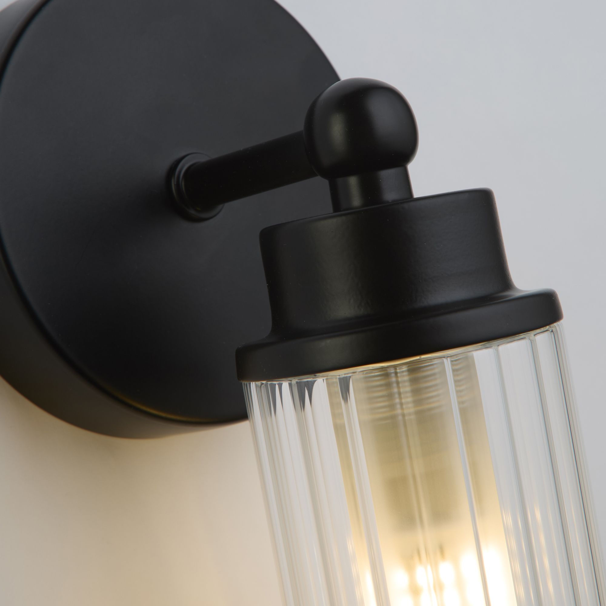 Close up of the matt black gimbal fitting and ribbed glass shade on the Searchlight Imperial wall light, bulb lit