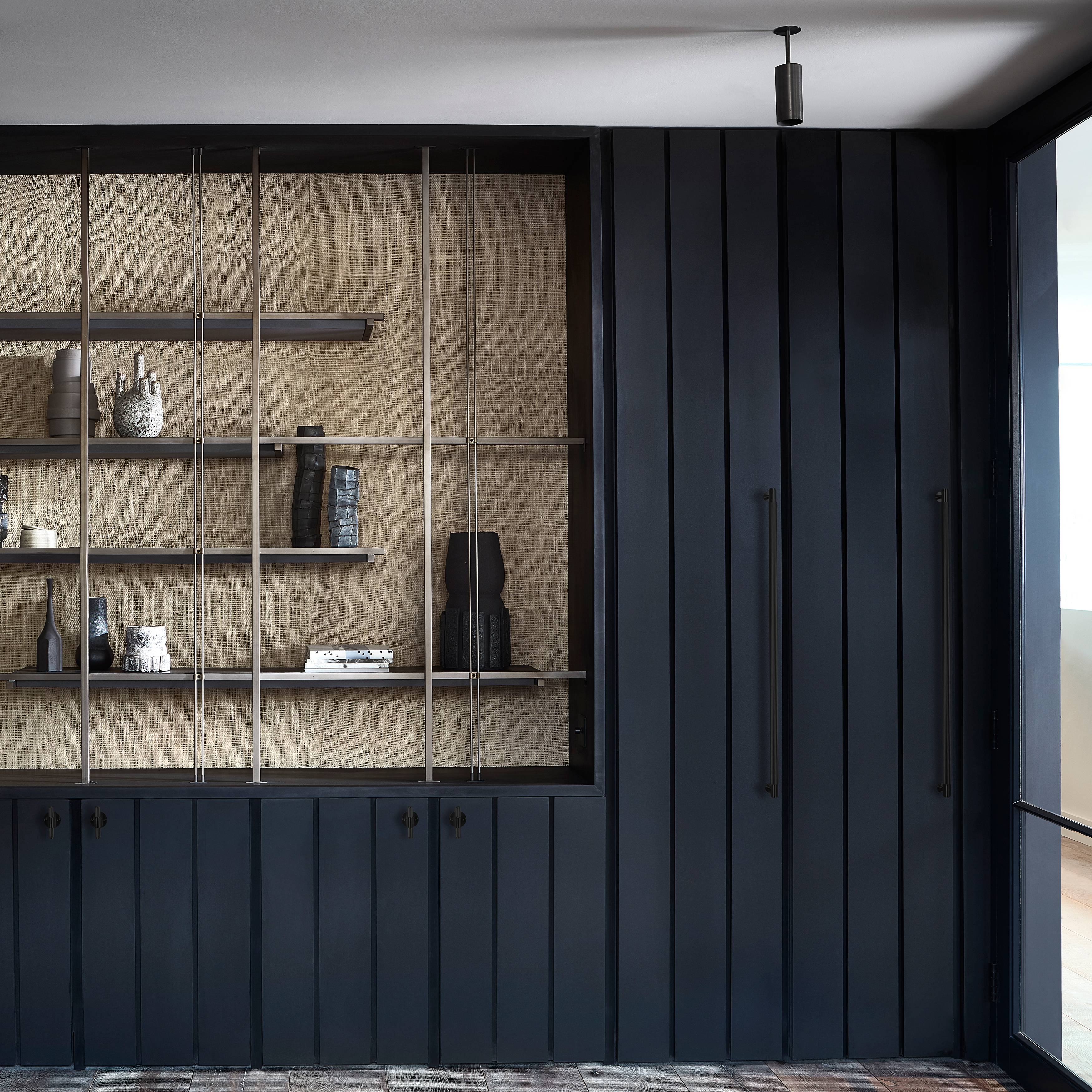 Open cane backed shelving with ceramics beside a dark wardrobe fitted with knurled pull bars
