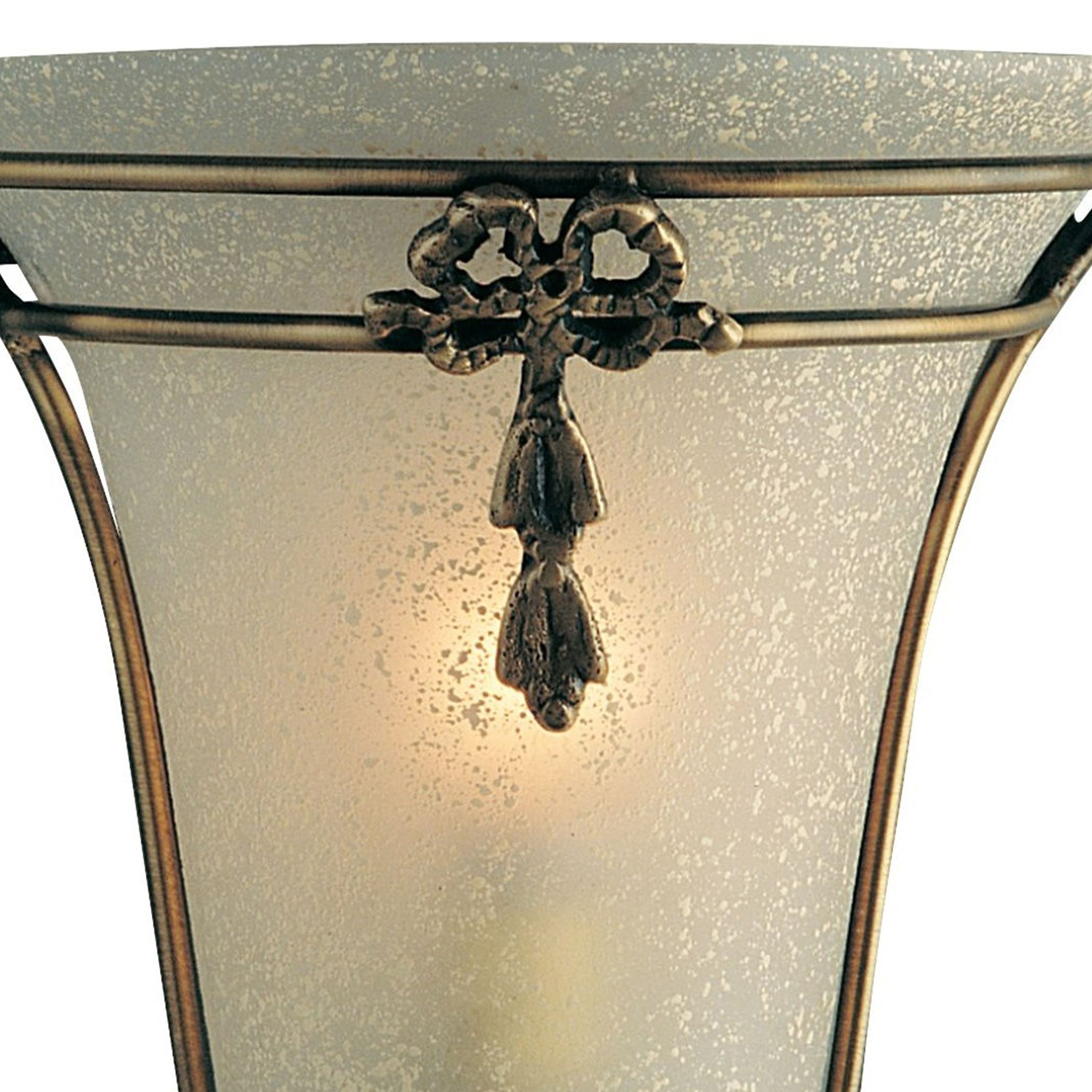 Close up of the Nashville wall light's antique brass ribbon motif and hanging finial against the frosted scavo glass shade