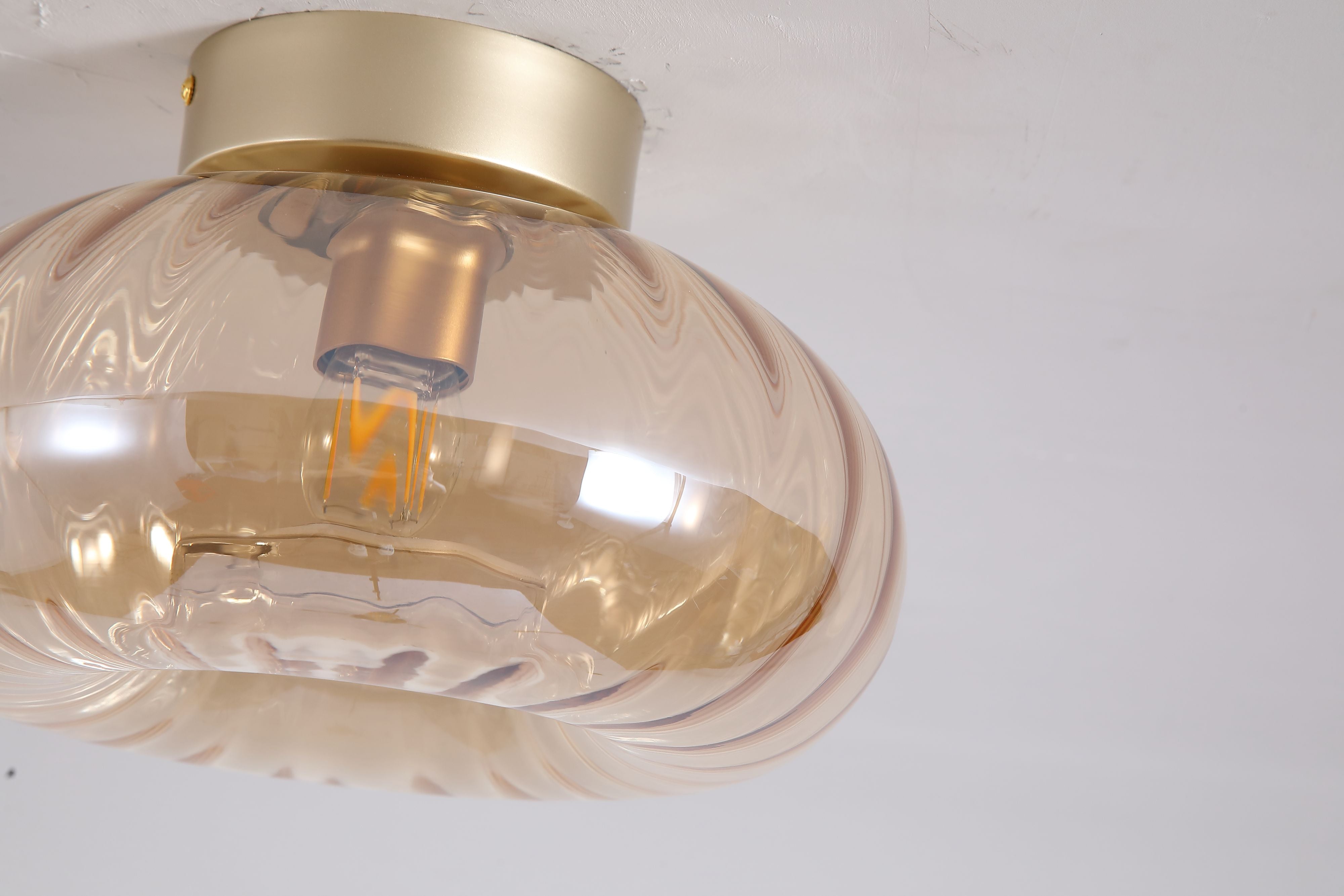 Close up of the ribbed amber glass shade and gold fitting on the Searchlight Celestial flush ceiling light, showing the lit bulb inside