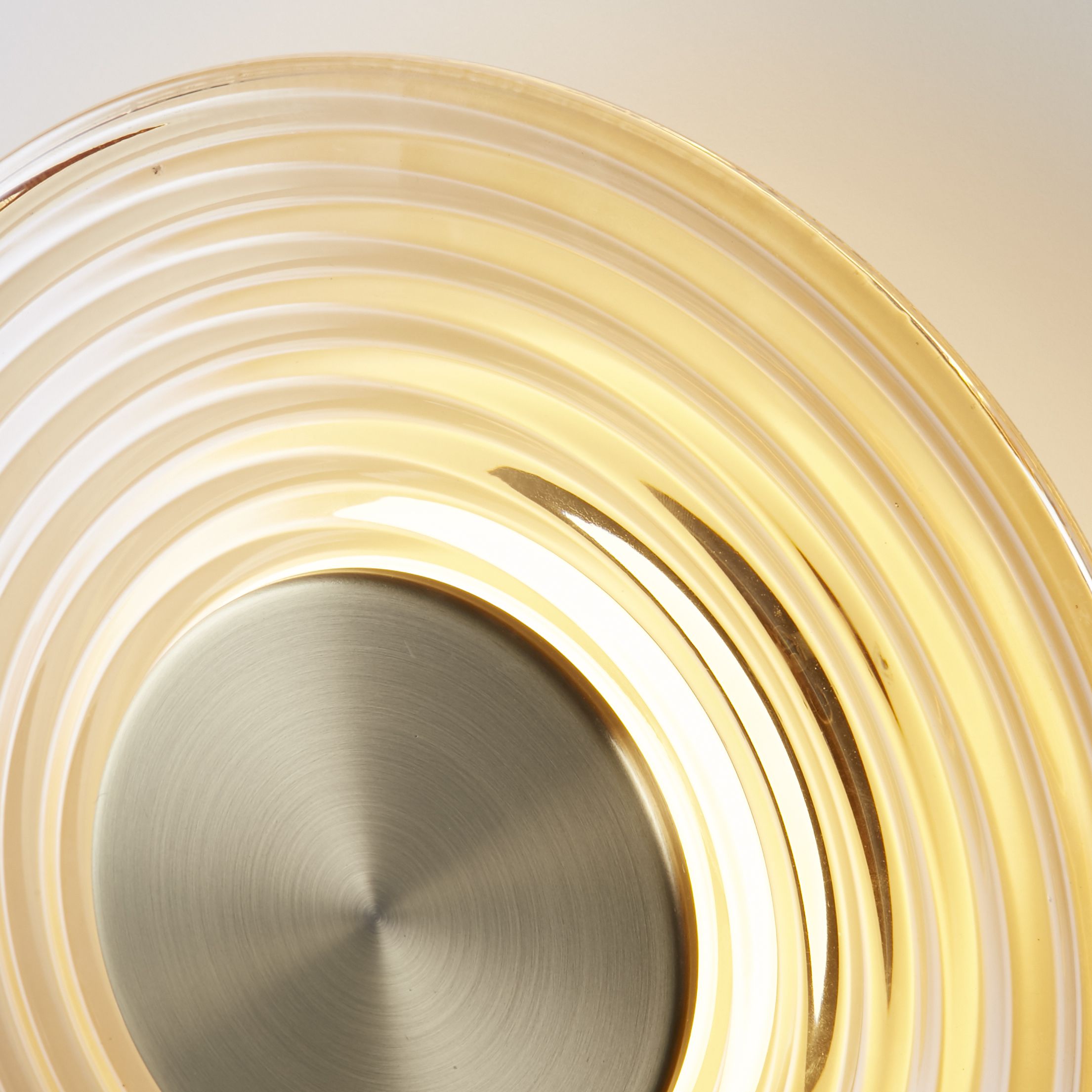 Close up detail of the Cleo wall light's antique brass centre disc and ribbed amber glass shade