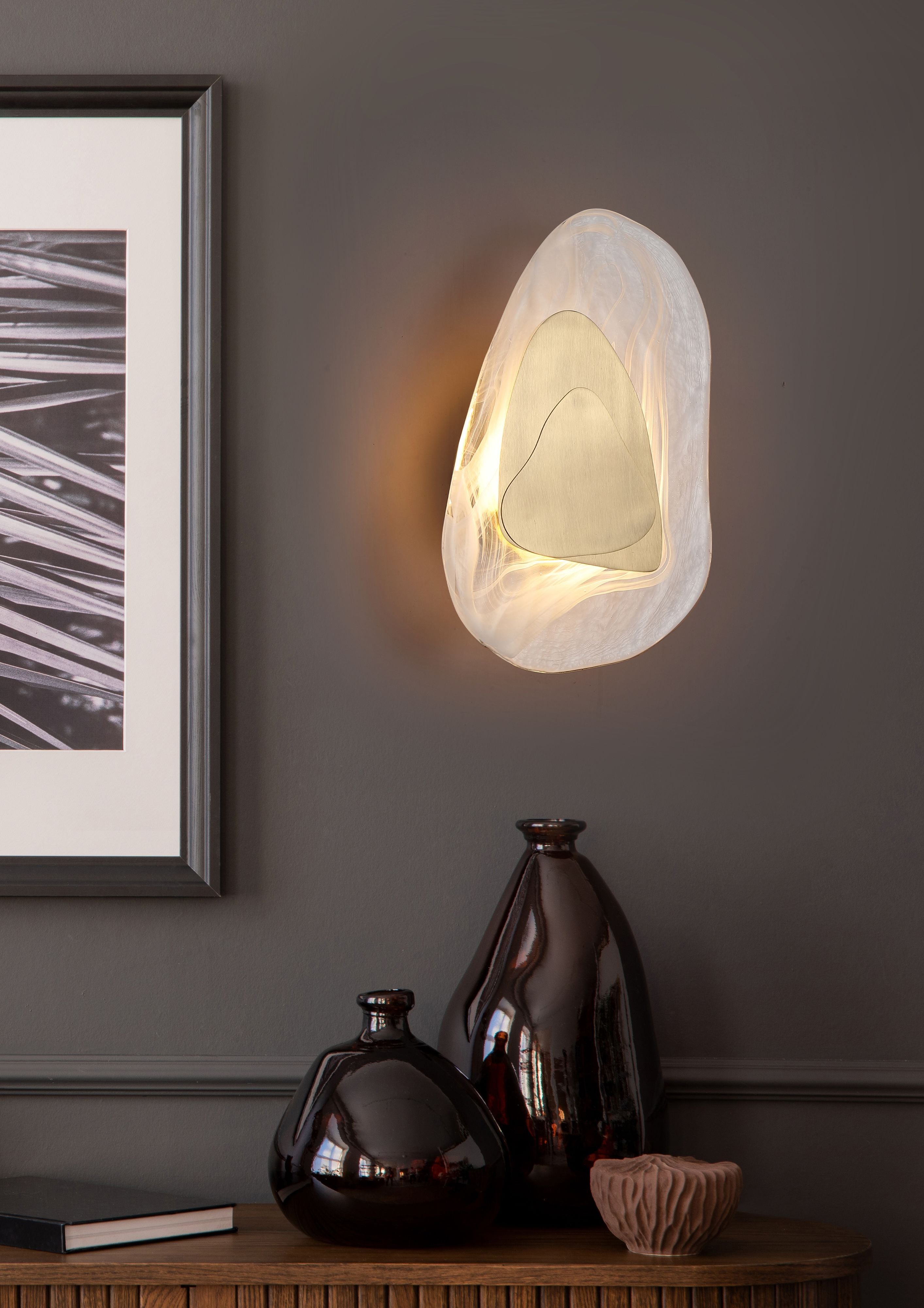 Destiny LED wall light in brass installed on a wall above a dark console table with framed prints and ceramic vases