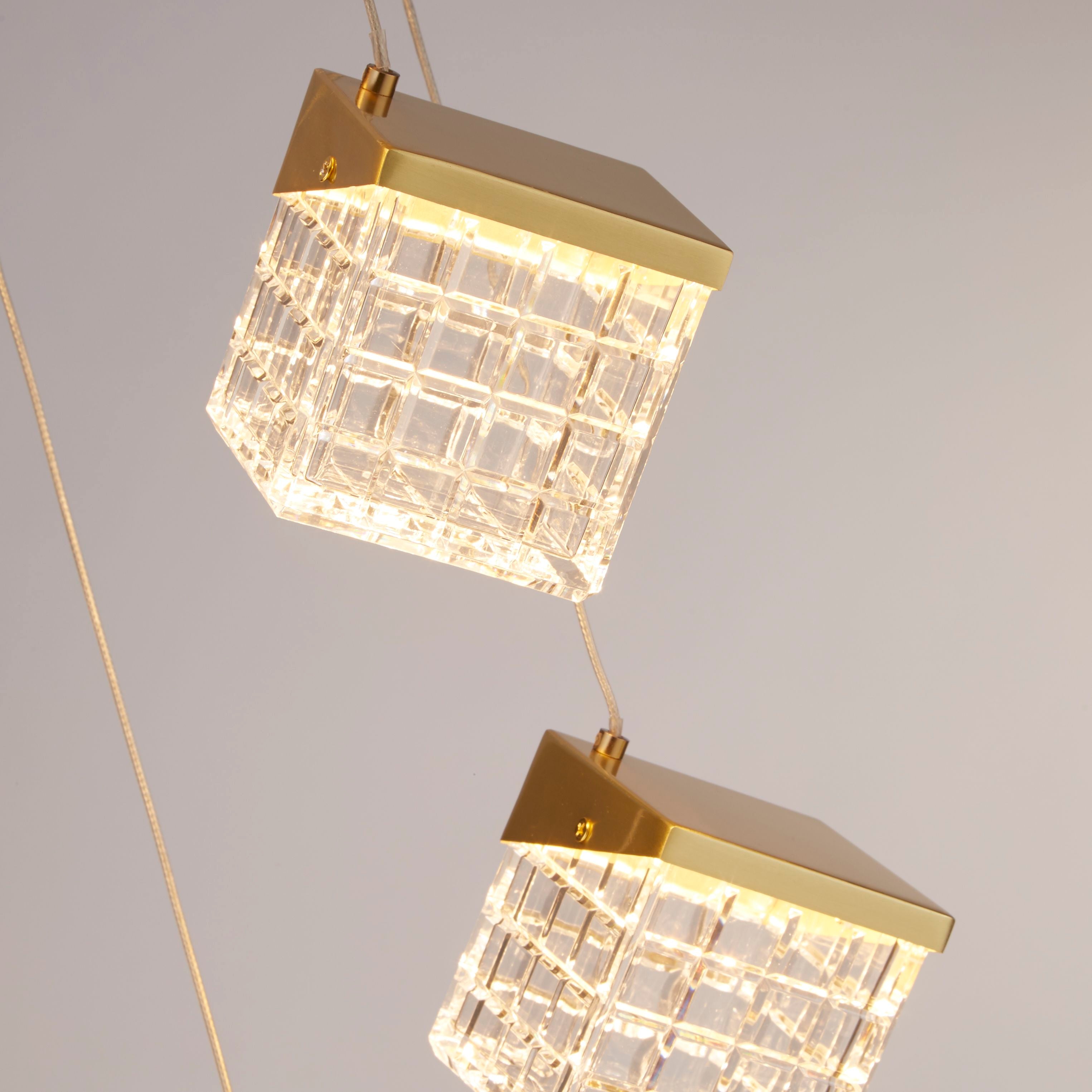 Close up of two Cuboid pendant cube shades in satin brass, showing the faceted cut acrylic grid pattern and brass corner caps lit from within