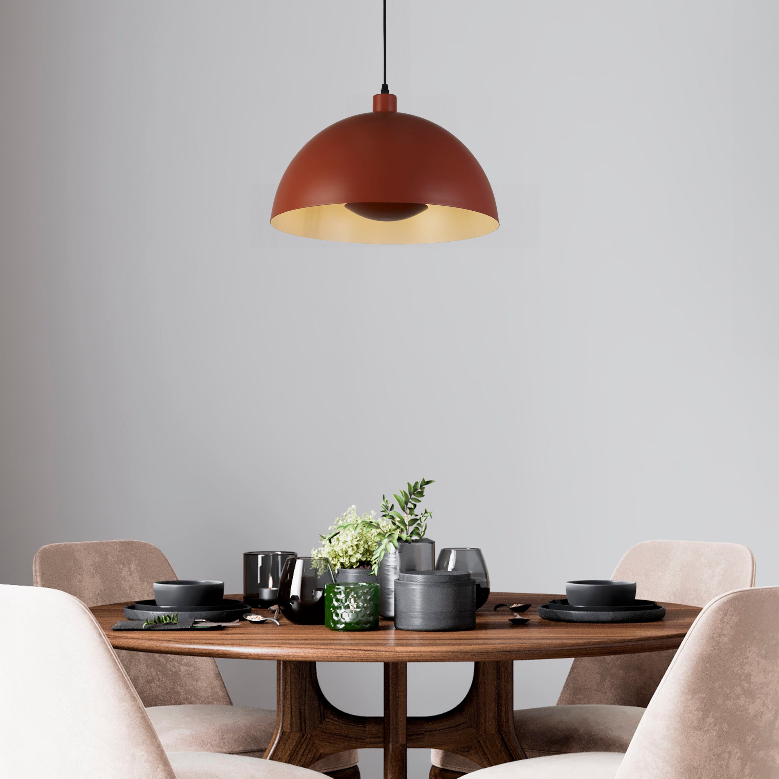 Searchlight Mars pendant in burnt orange metal hung above a dark wood dining table set with black tableware and greenery