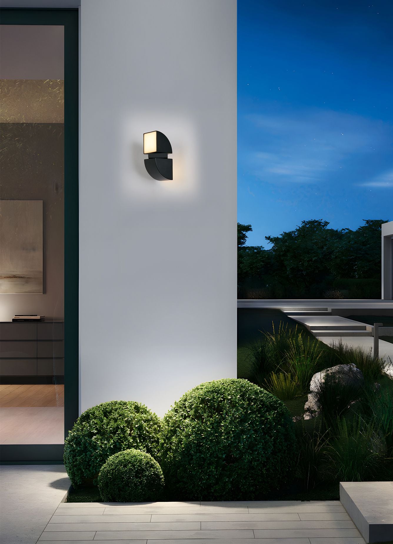 Dakota black outdoor wall light installed on an exterior wall at night, casting warm light over a planted border