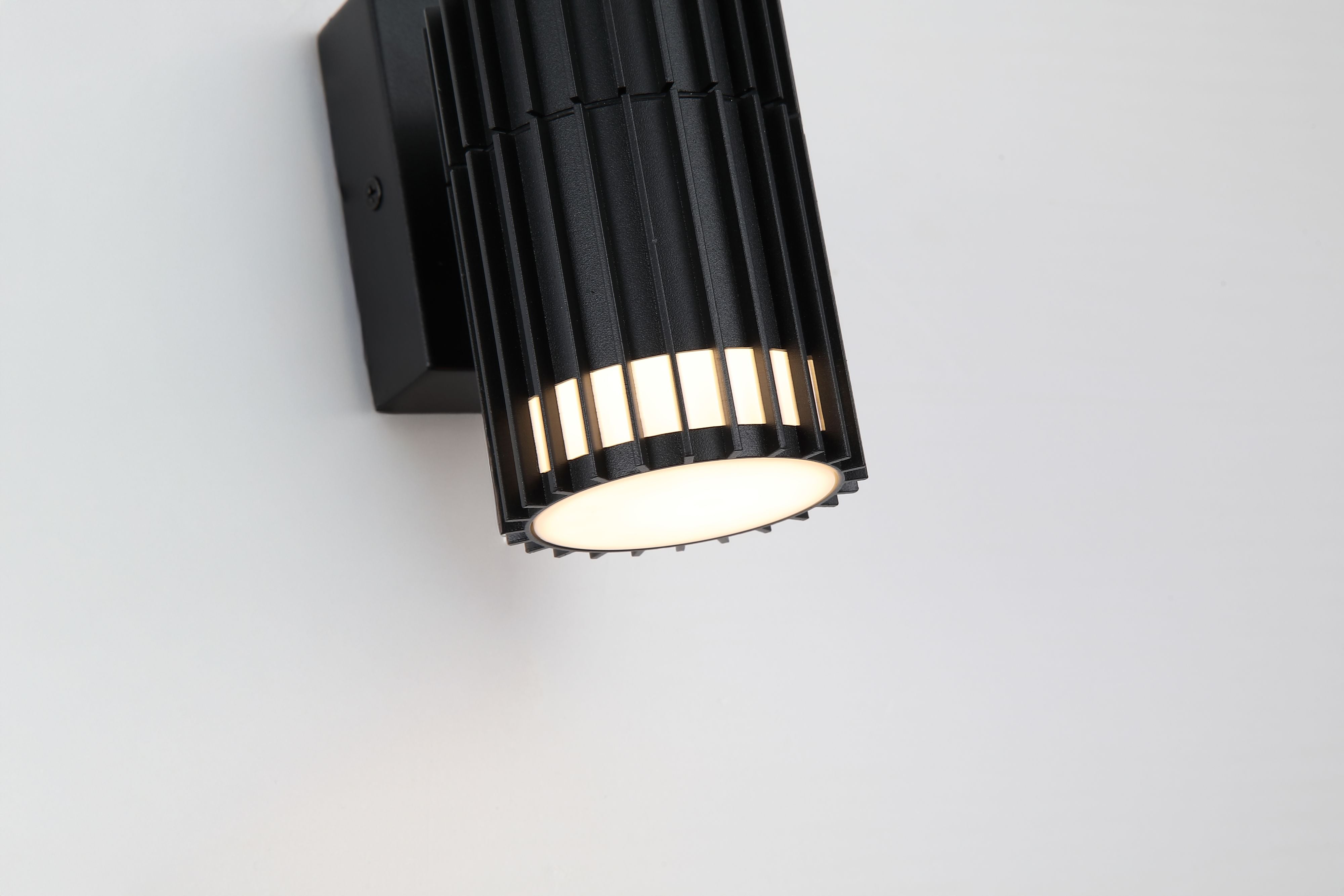 Close up angled view of the Detroit wall light showing light escaping between the vertical fins and the square wall plate.