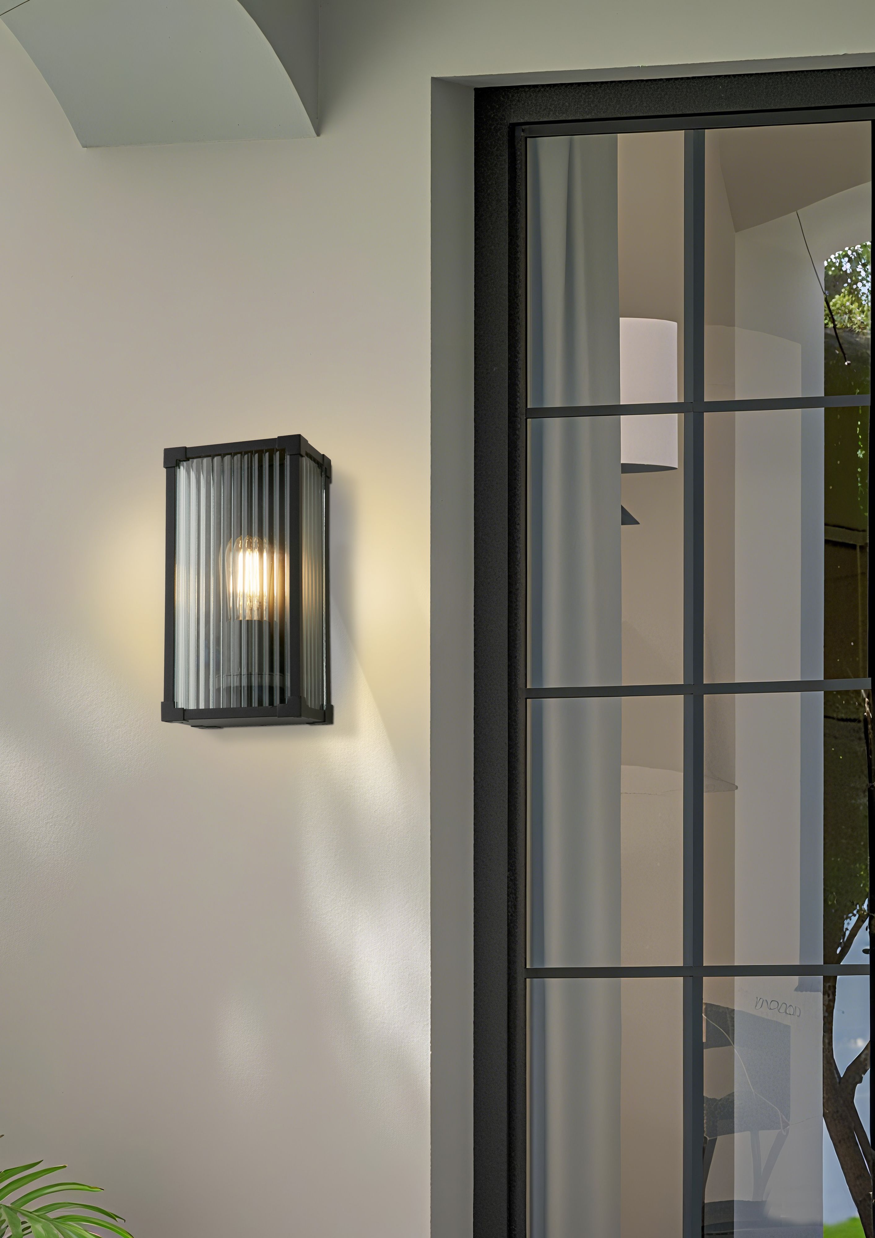 Cincinnati outdoor wall light installed and lit beside a glazed front door on a light rendered wall