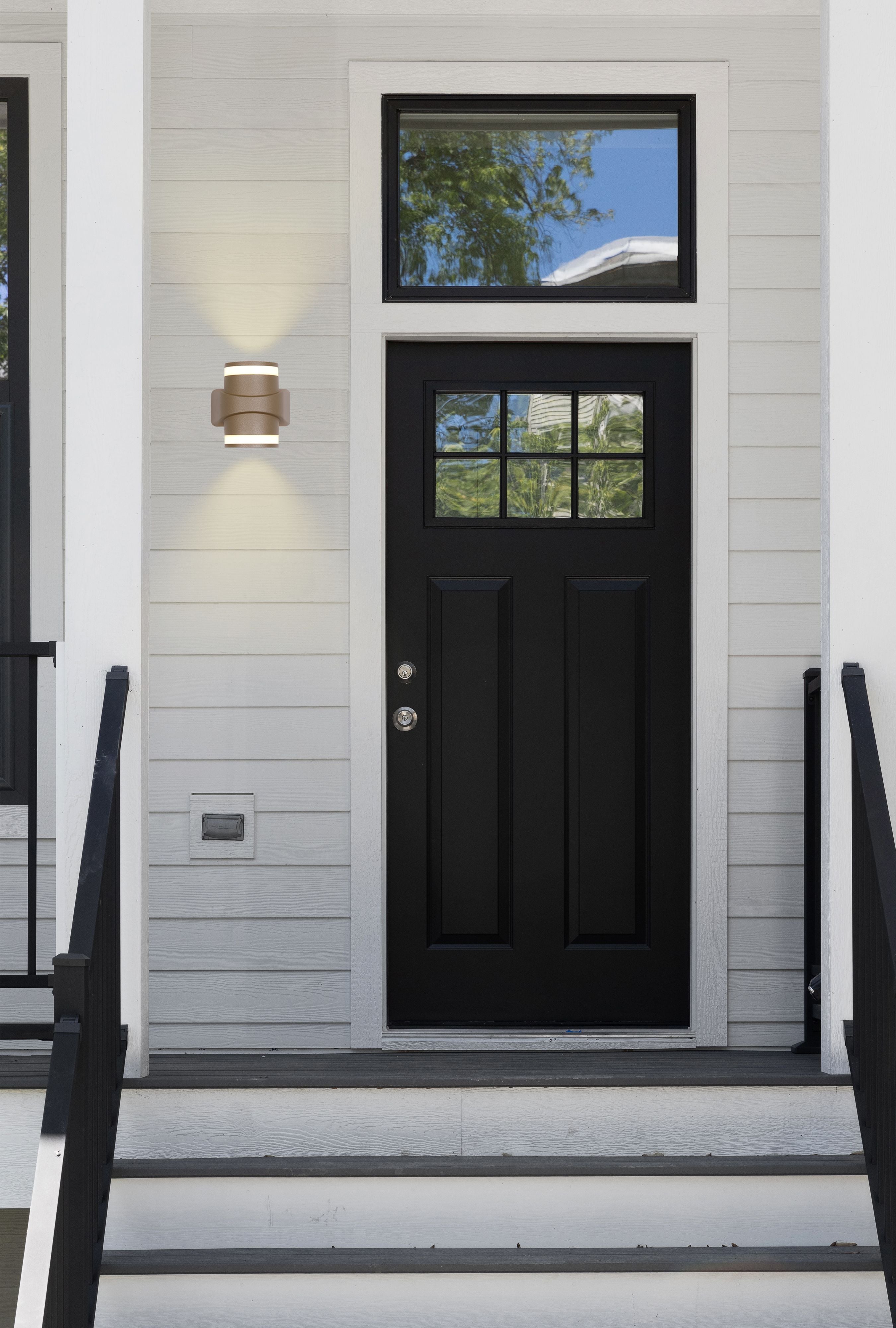 Grip LED outdoor wall light in gold installed beside a black front door, lit, on a light grey painted exterior wall