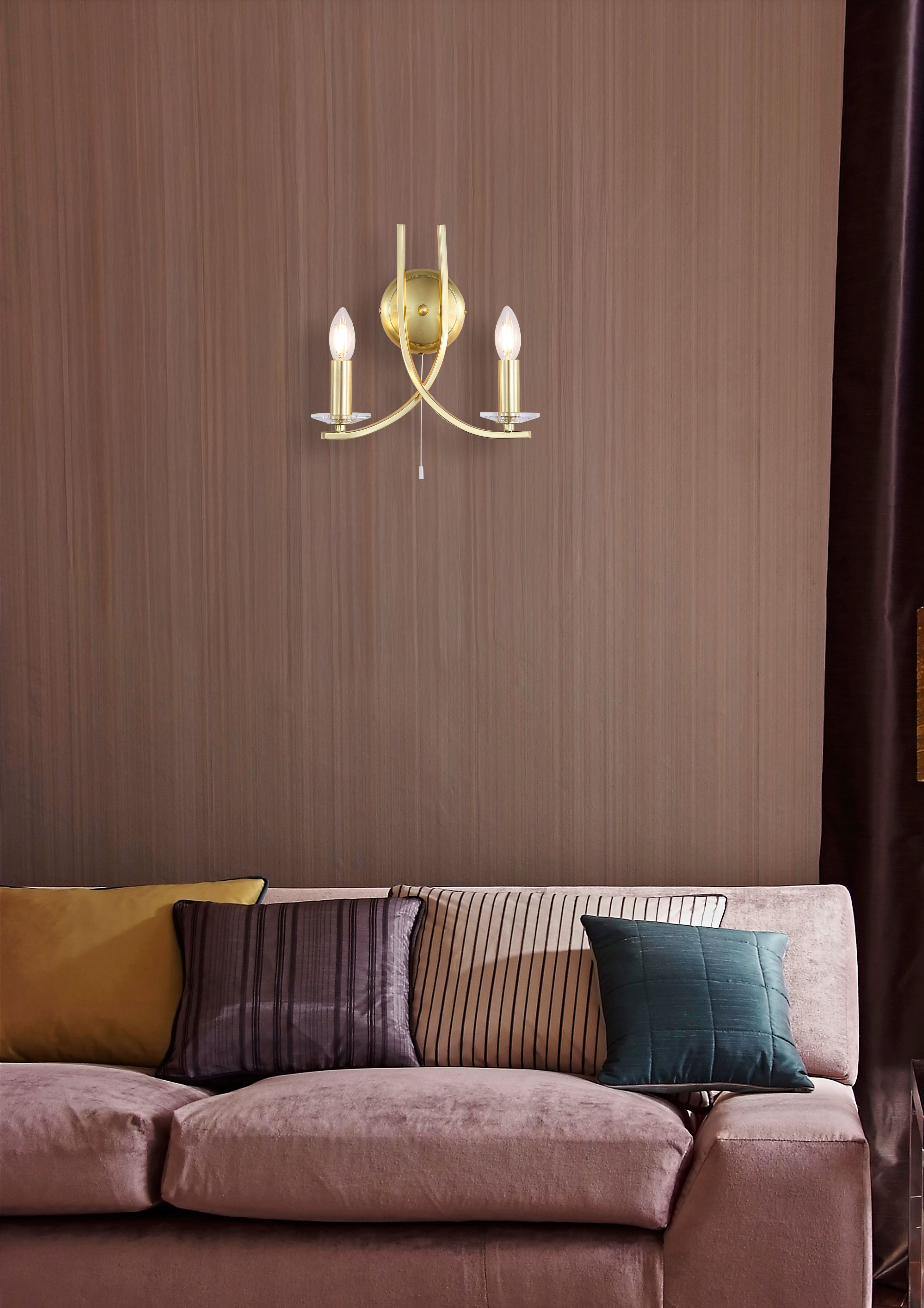 Searchlight Ascona 2 Light Wall Light in satin brass mounted above a mauve velvet sofa with striped and jewel toned cushions