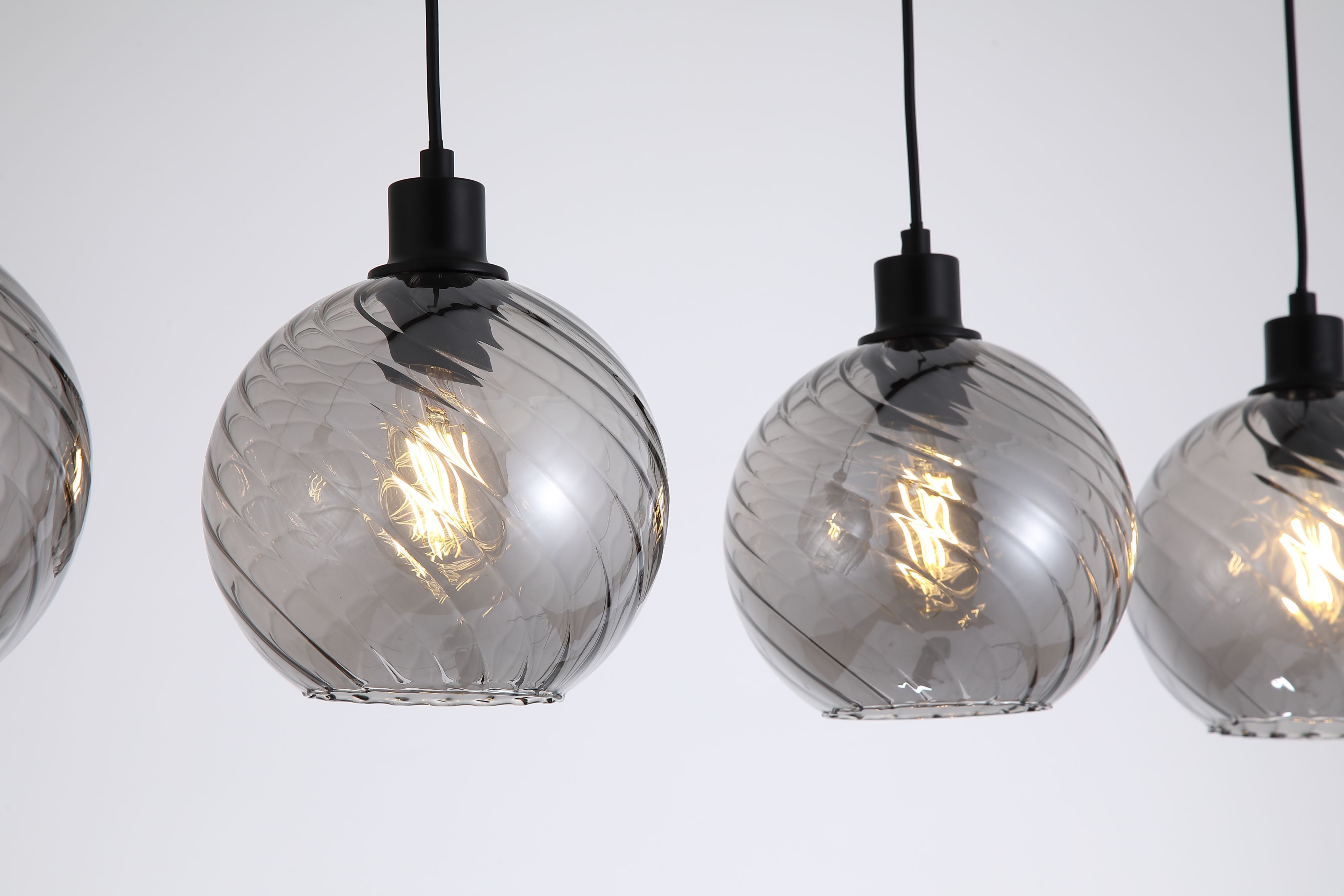Close up of the swirled ribbed texture on the smoked glass globe shades of the Radiance 4 Light Bar Pendant, showing the black fitting and filament bulb detail