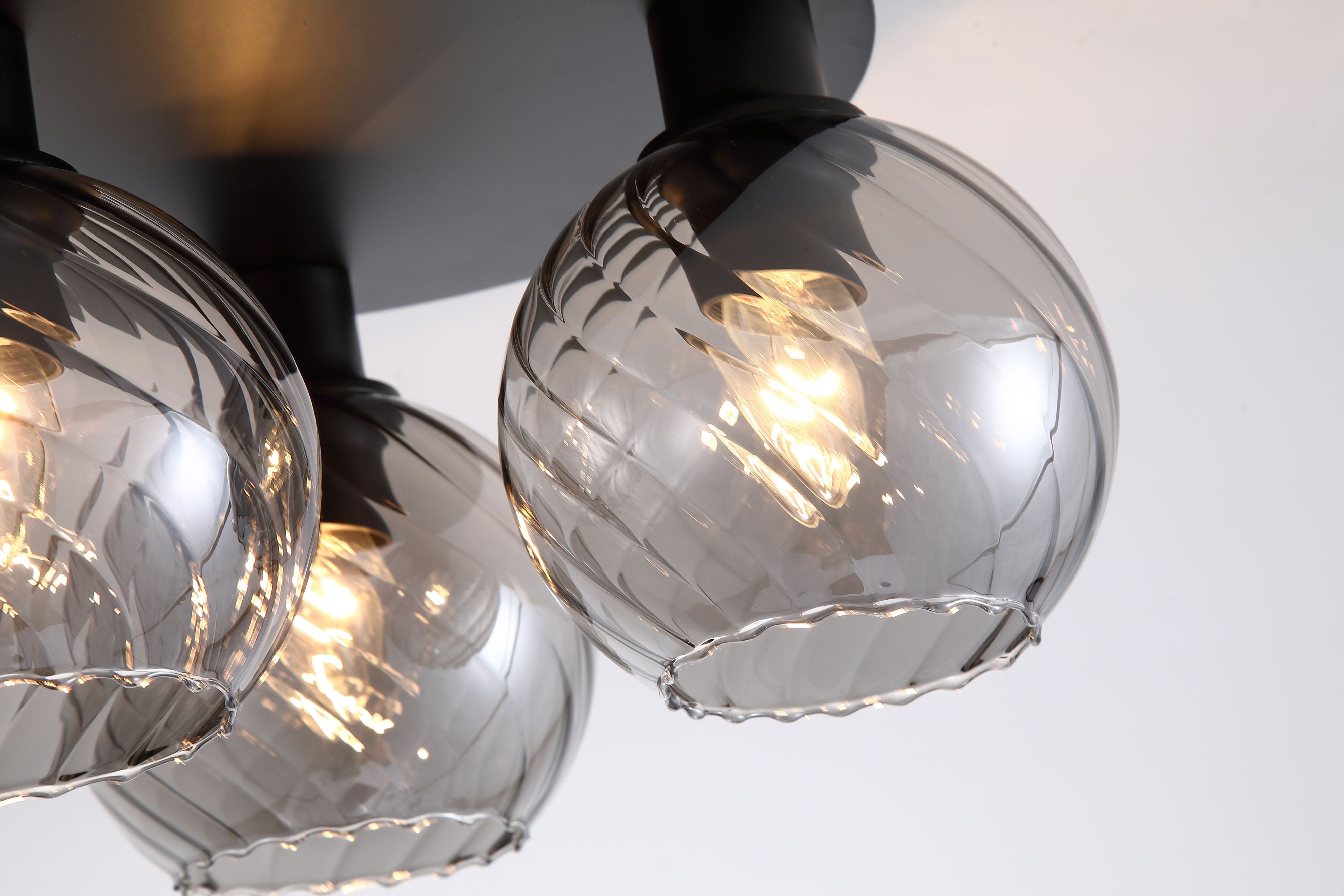 Close up of the swirled ribbed texture on the smoked glass globe shades of the Radiance 3 Light Flush, showing the black fitting and filament bulb detail
