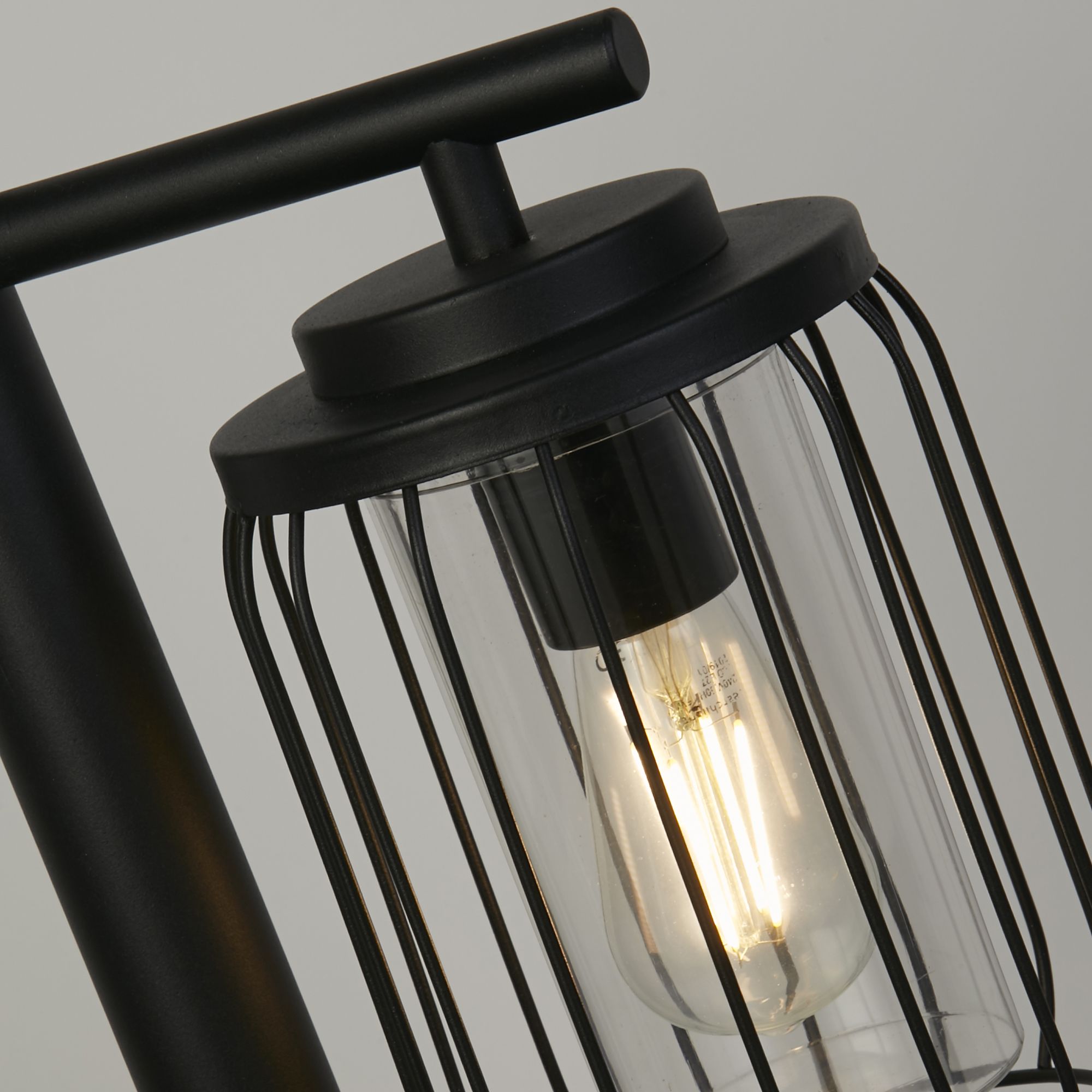 Close up of the Reed post light's wire cage lantern head, clear polycarbonate diffuser and lit filament style bulb.
