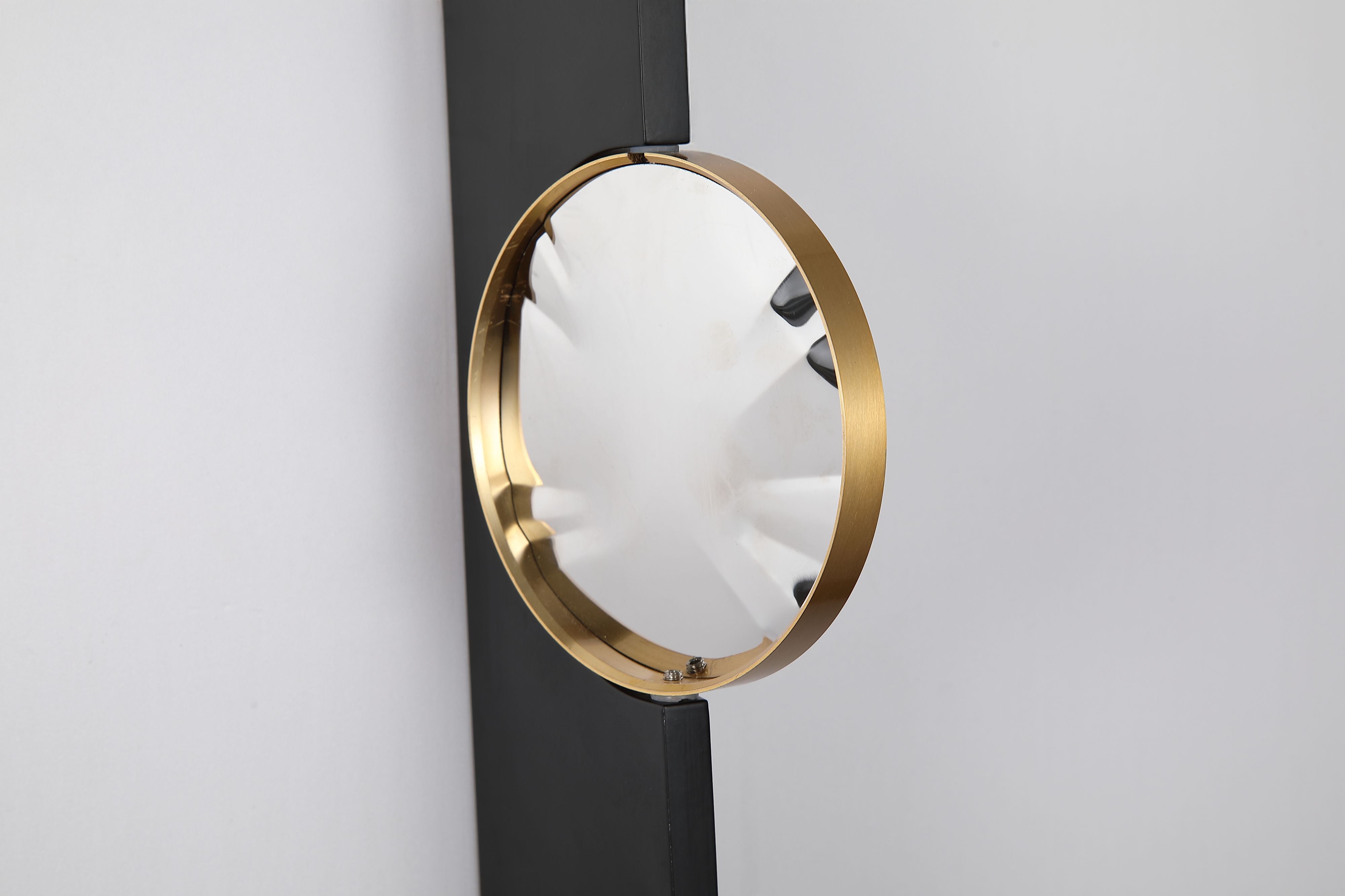 Close up of the Searchlight Shield LED Wall Light showing the brushed brass disc at an angle, with its mirror like finish and the small tilt mounting screws visible