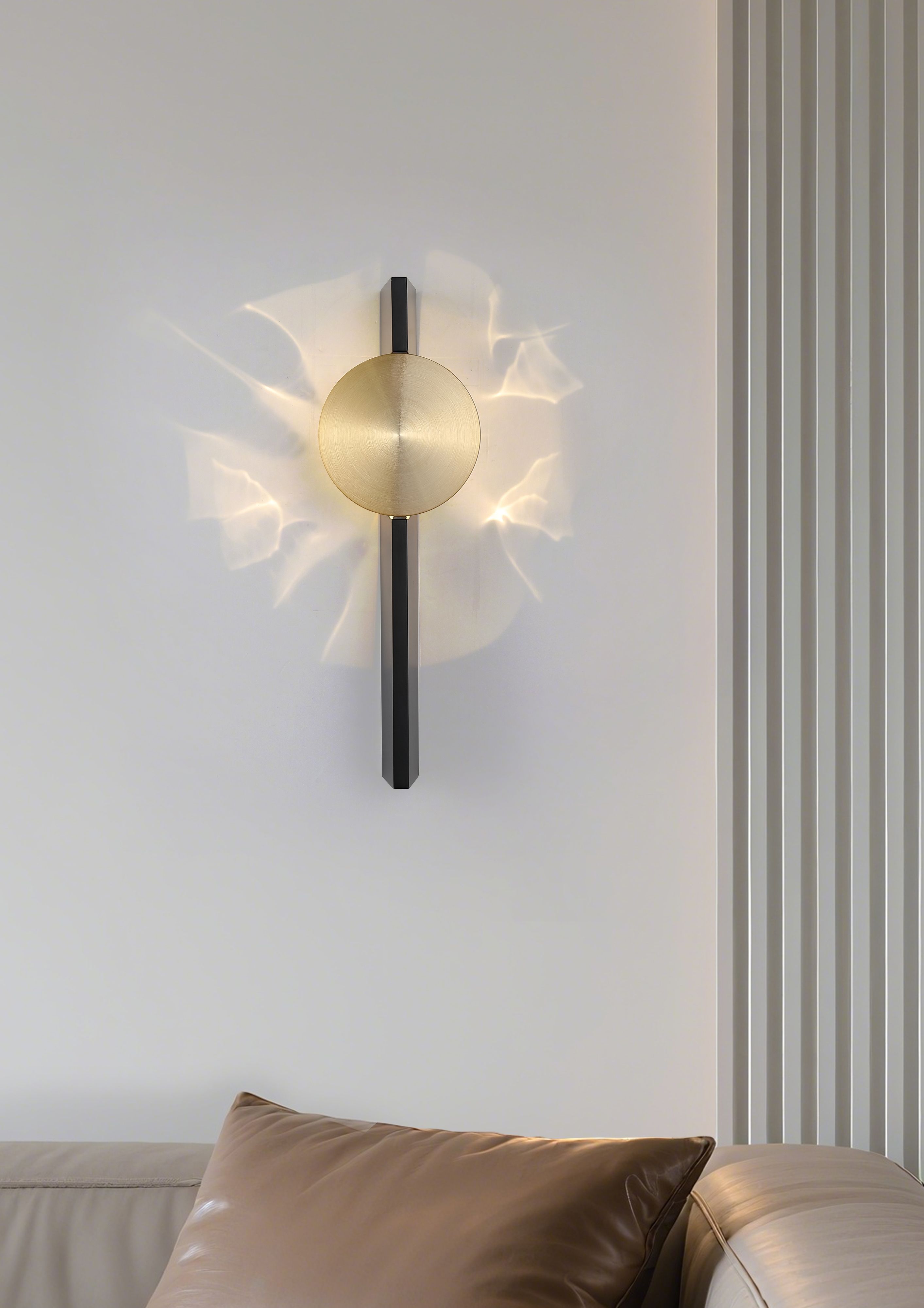 Searchlight Shield LED Wall Light in sand black and brass, mounted above a sofa with leather cushions, lit and casting an angular fractured wash of light across the wall