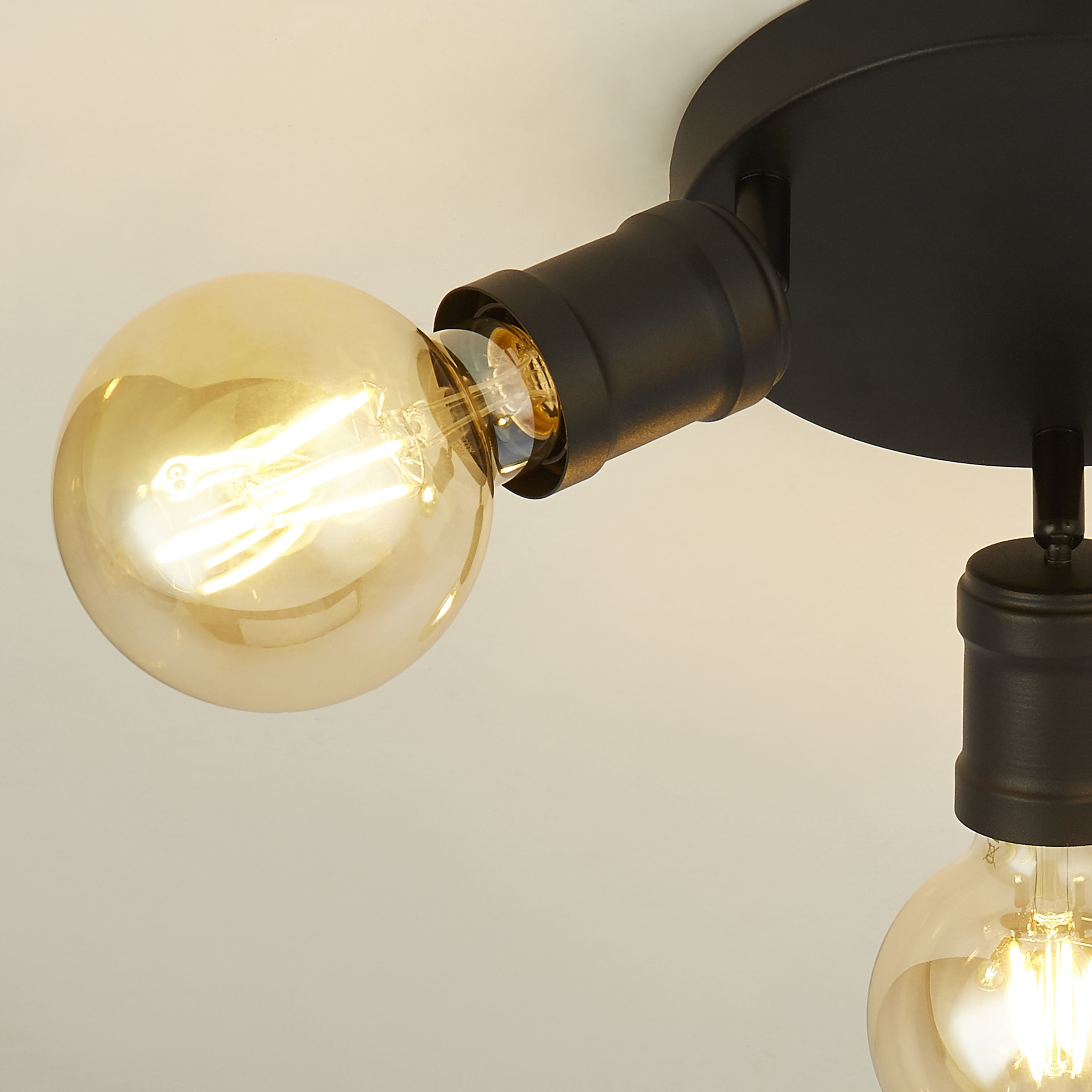 Close up of the Searchlight Dance flush ceiling light showing one adjustable black arm holding a lit vintage style globe bulb