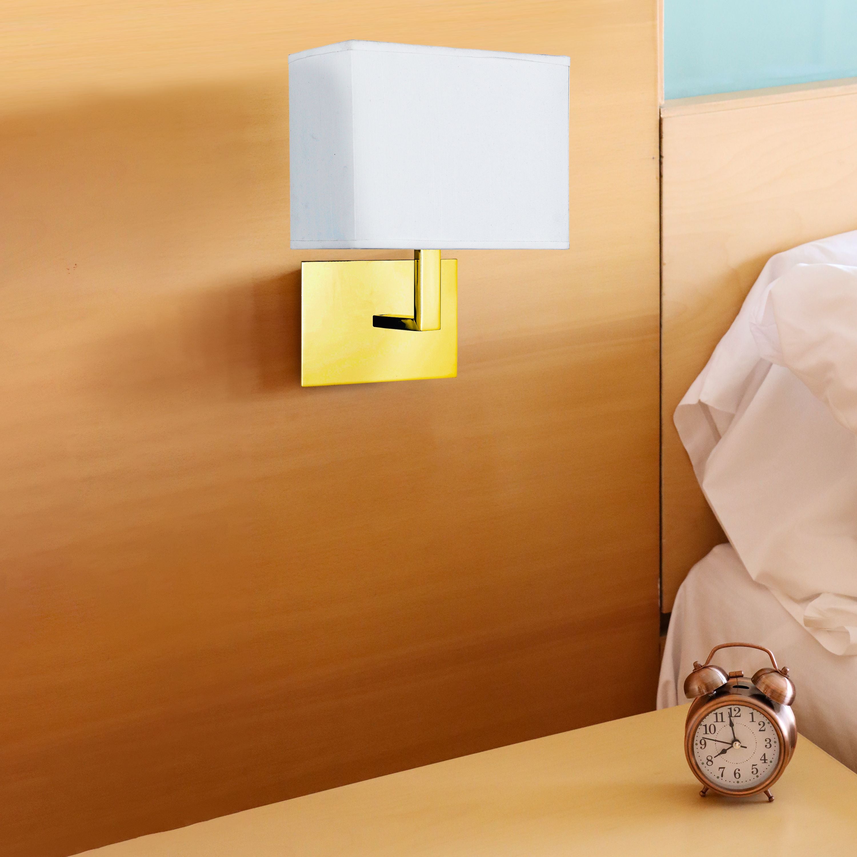 Searchlight Hotel Wall Light in satin brass mounted above a bedside table with an alarm clock, on a wood panelled wall
