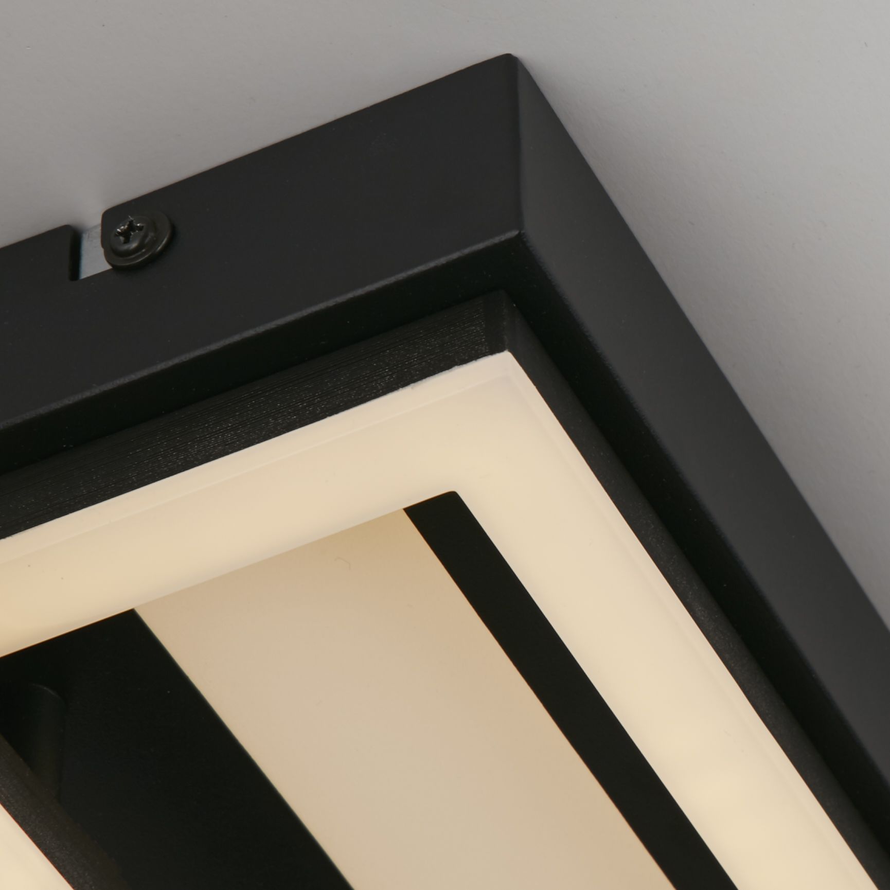 Close up of the Ovaloid flush light's black frame corner, showing the acrylic diffuser strip, ceiling mounting screw and iron construction