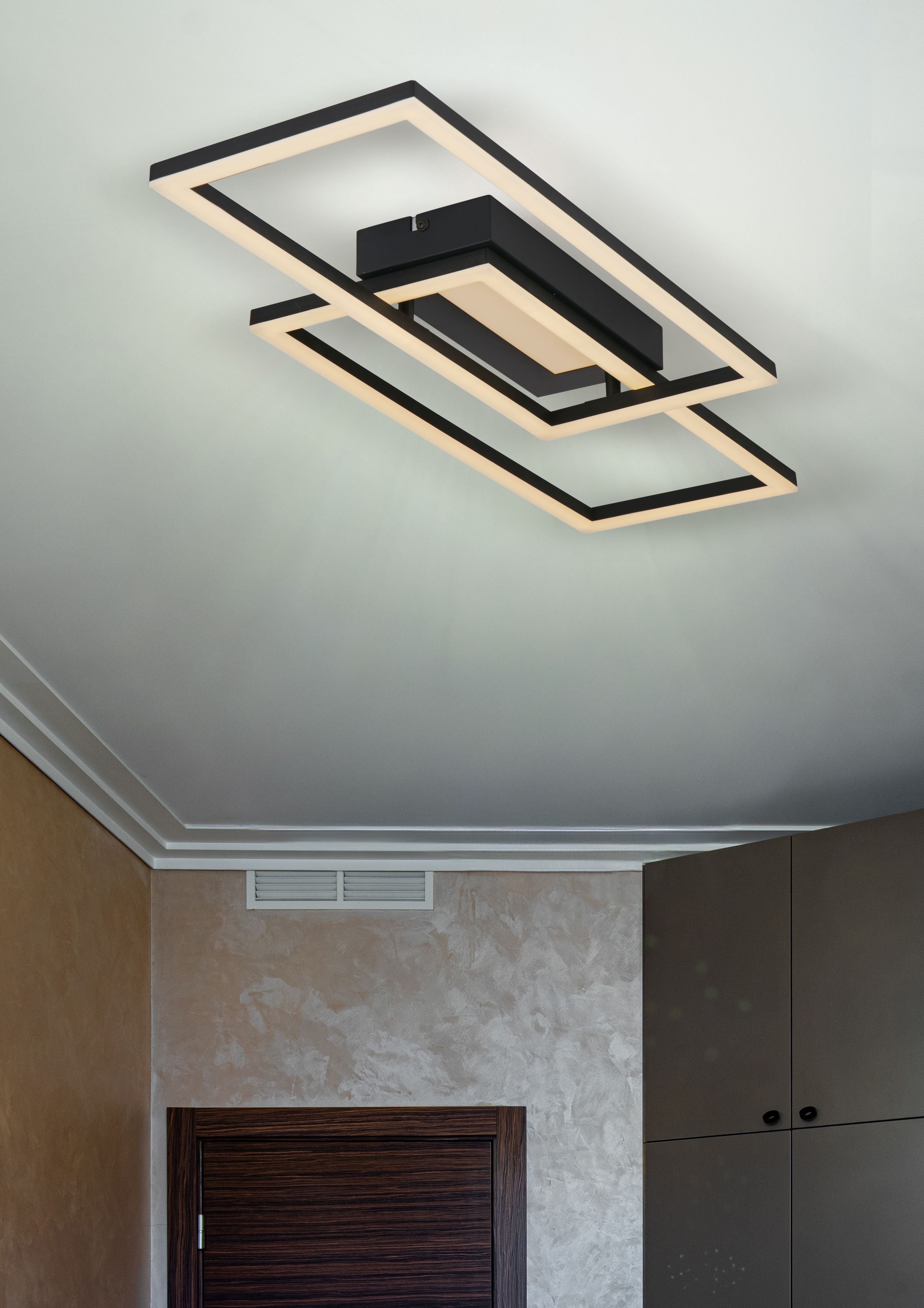 Ovaloid LED flush light installed on a bedroom ceiling in matt black, illuminated with warm white light above a wardrobe and door