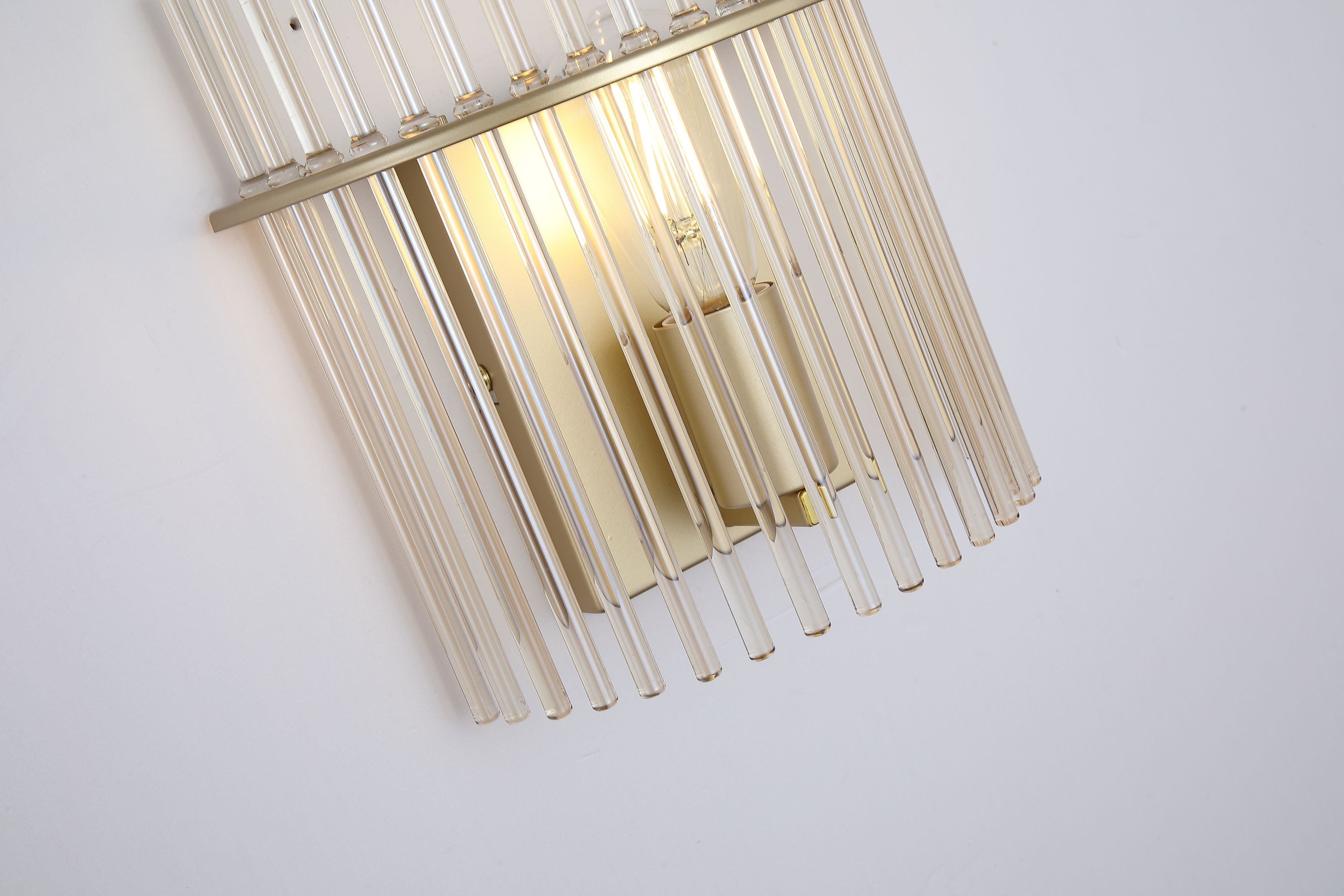 Close up angled detail of the Swizzle wall light showing the champagne tinted glass rods, gold backplate and lit bulb