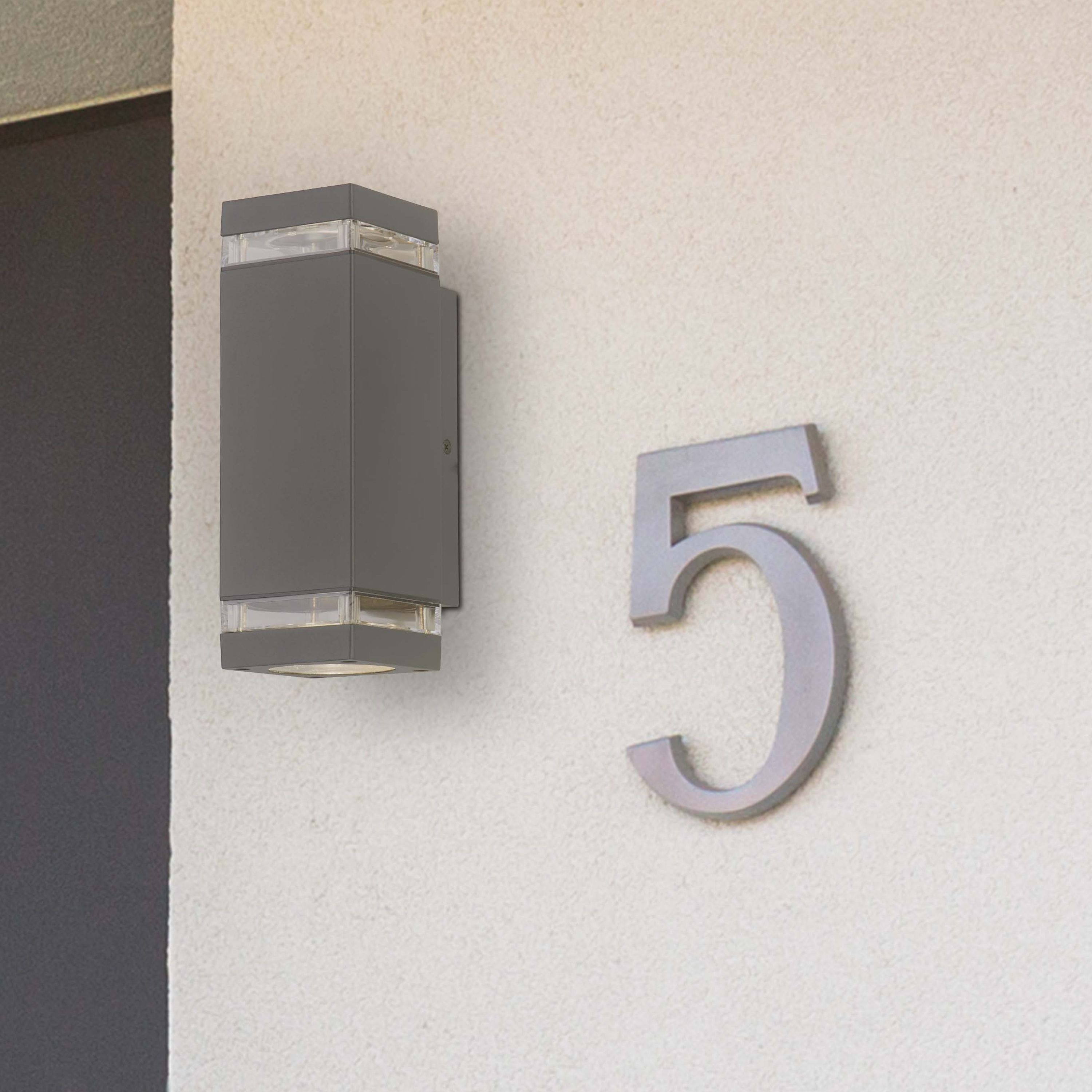 Searchlight Houston grey outdoor wall light mounted on a beige stucco wall next to a house number 5 plaque, switched on