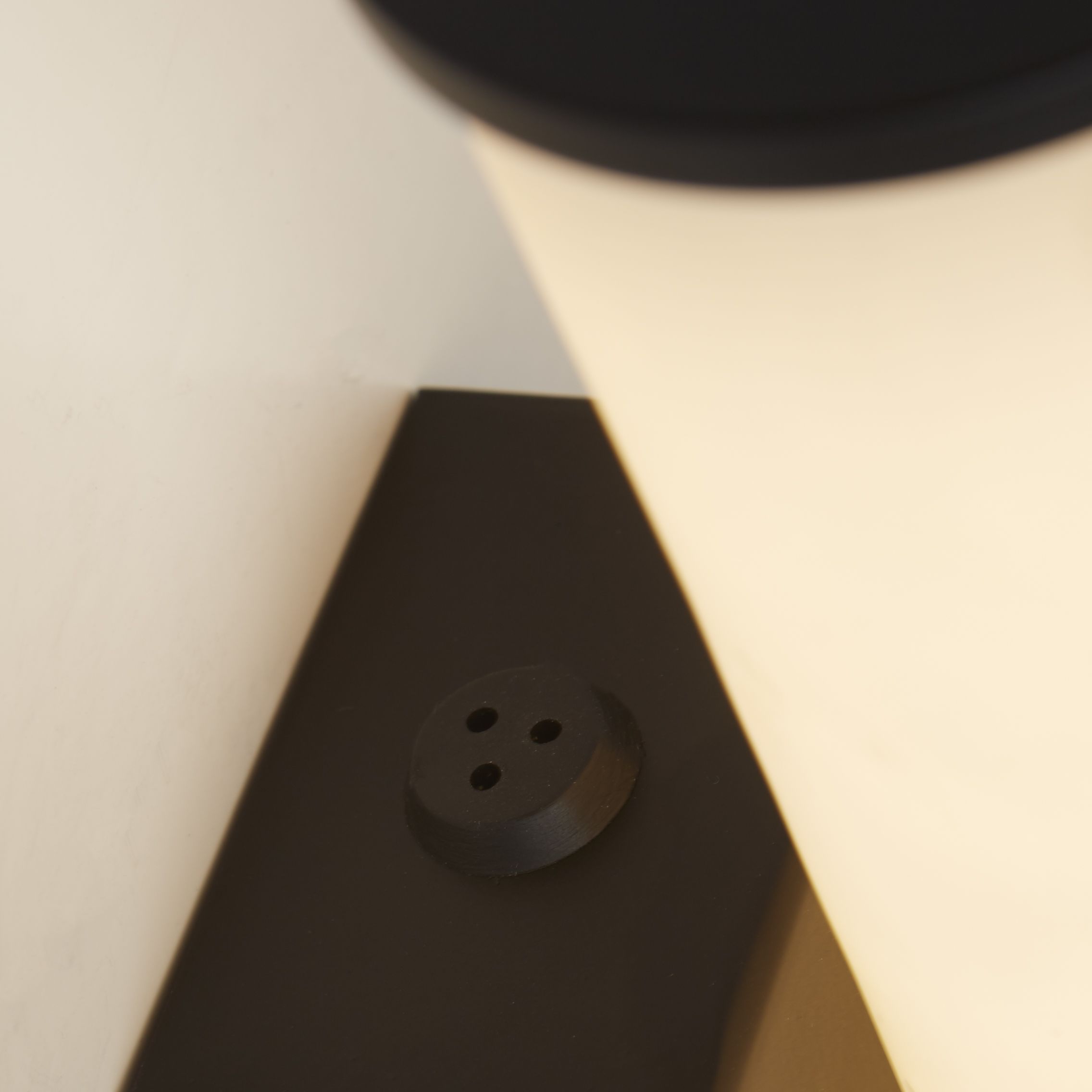 Close up of the Wales wall light's matt black rectangular back plate and fixing screw