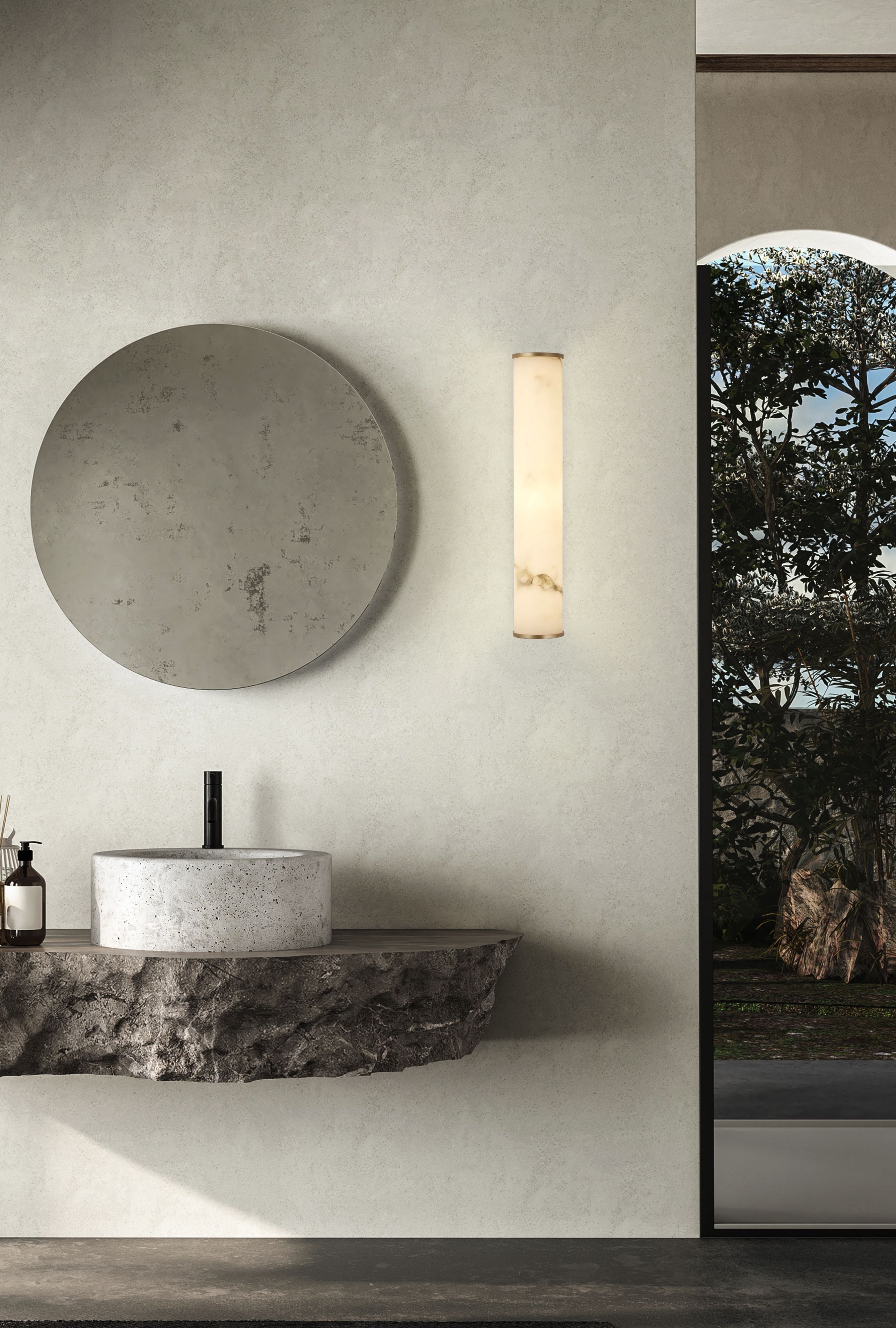 A pair of matt gold Wales wall lights mounted either side of a round gold framed mirror above a wood vanity in a styled bathroom
