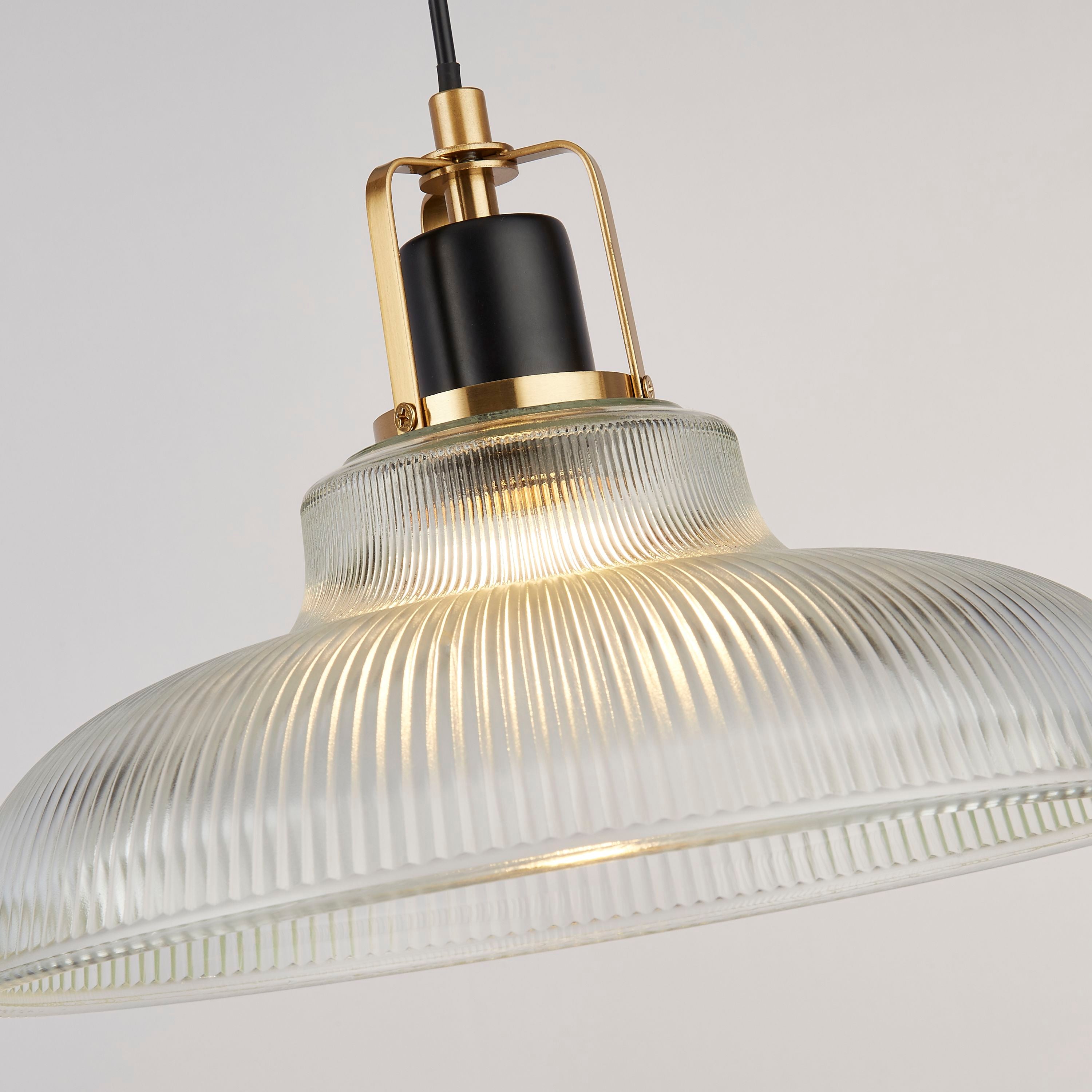 Close up of the Glossop pendant's black lamp holder and brass cage above the ribbed glass shade, lit