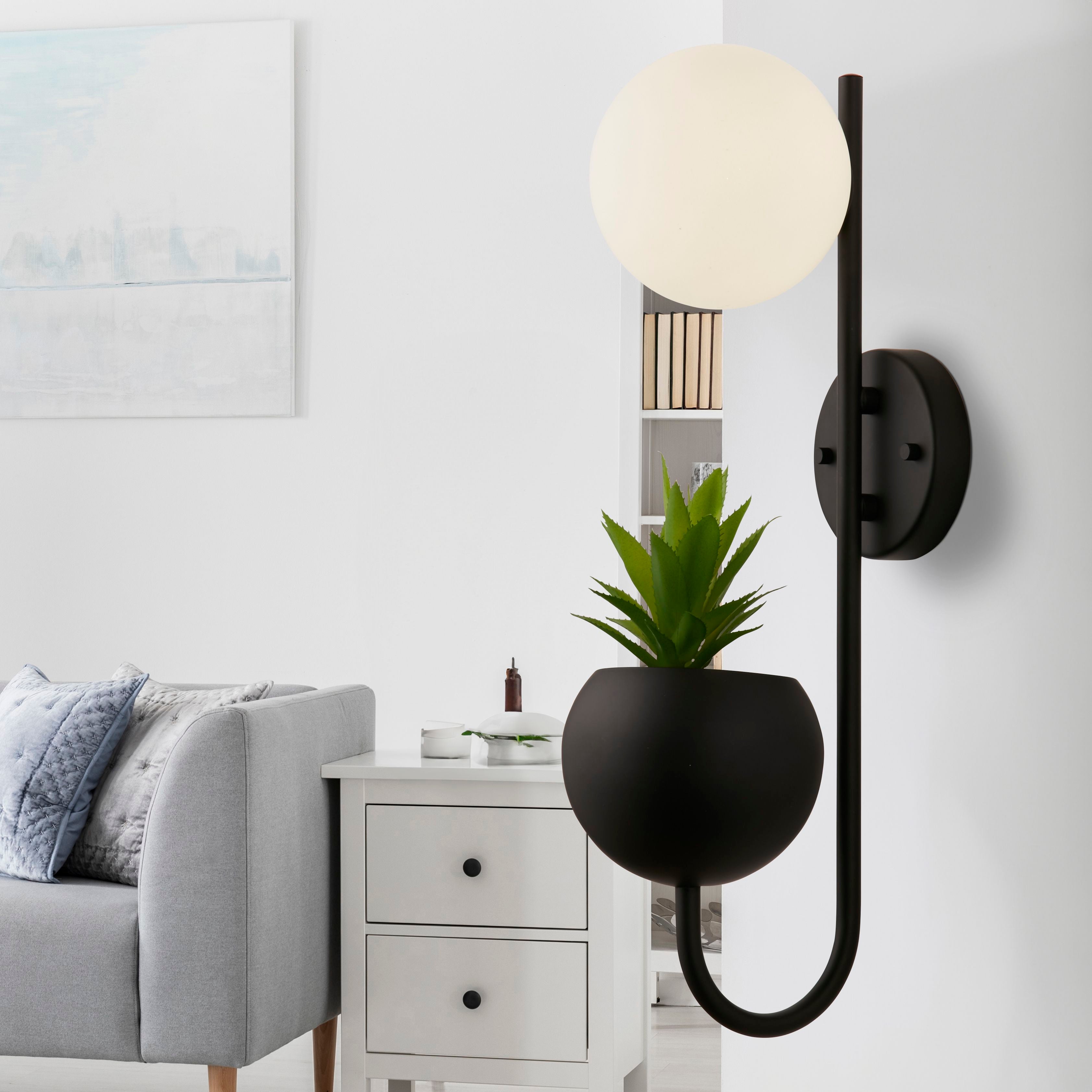 Searchlight x Lunar Wall Light in black mounted above a white bedside cabinet next to a grey sofa, with the opal globe lit
