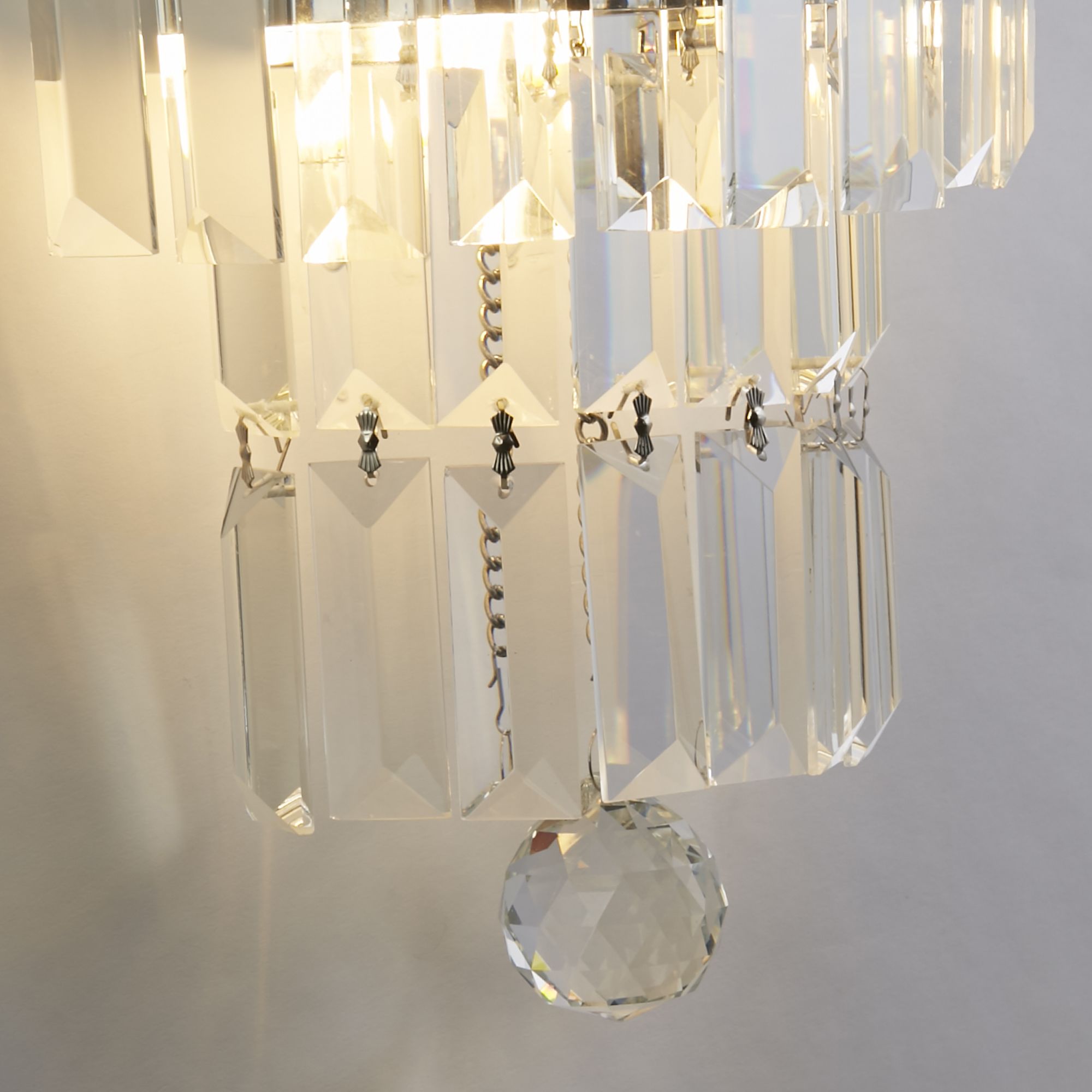 Close up of the Empire wall light's clear crystal prisms and chrome frame, showing the faceted glass detail lit from within