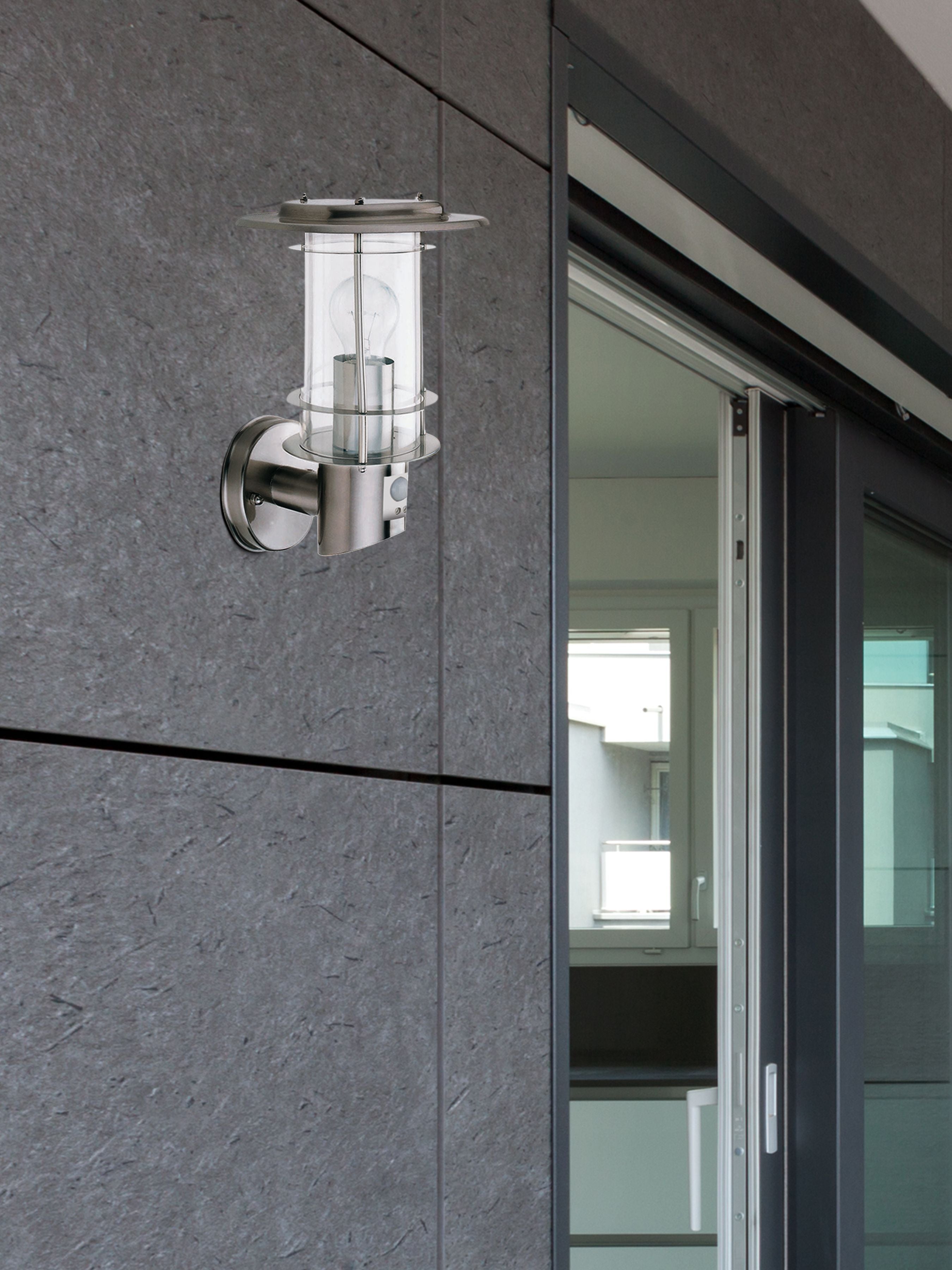 Edgeware stainless steel wall light mounted on a dark stone clad exterior wall beside a modern sliding glass door, lit