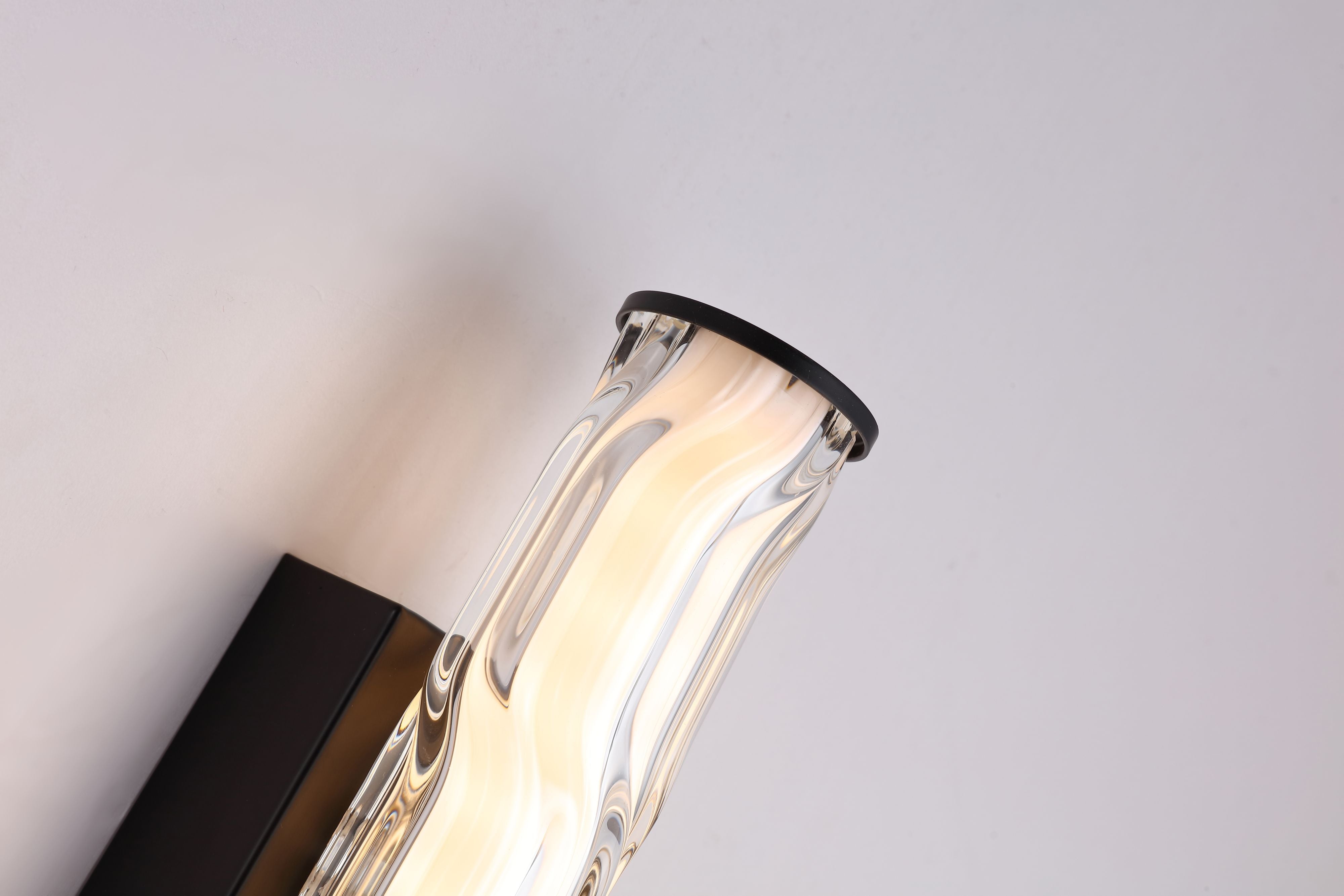 Close up of the Vibrate wall light's wave ridge glass texture and matt black end cap, lit from within