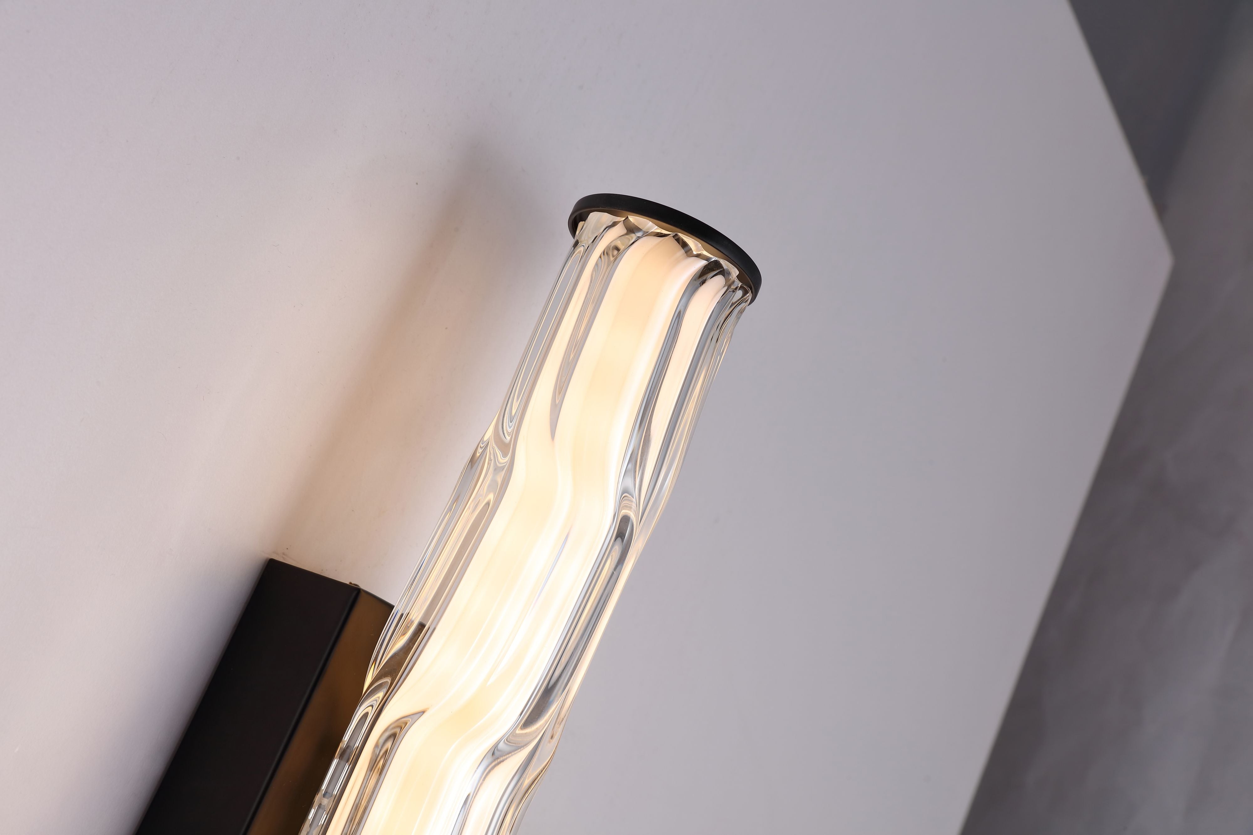 Close up of the Vibrate wall light's top end cap in matt black, showing the wave ridged glass texture