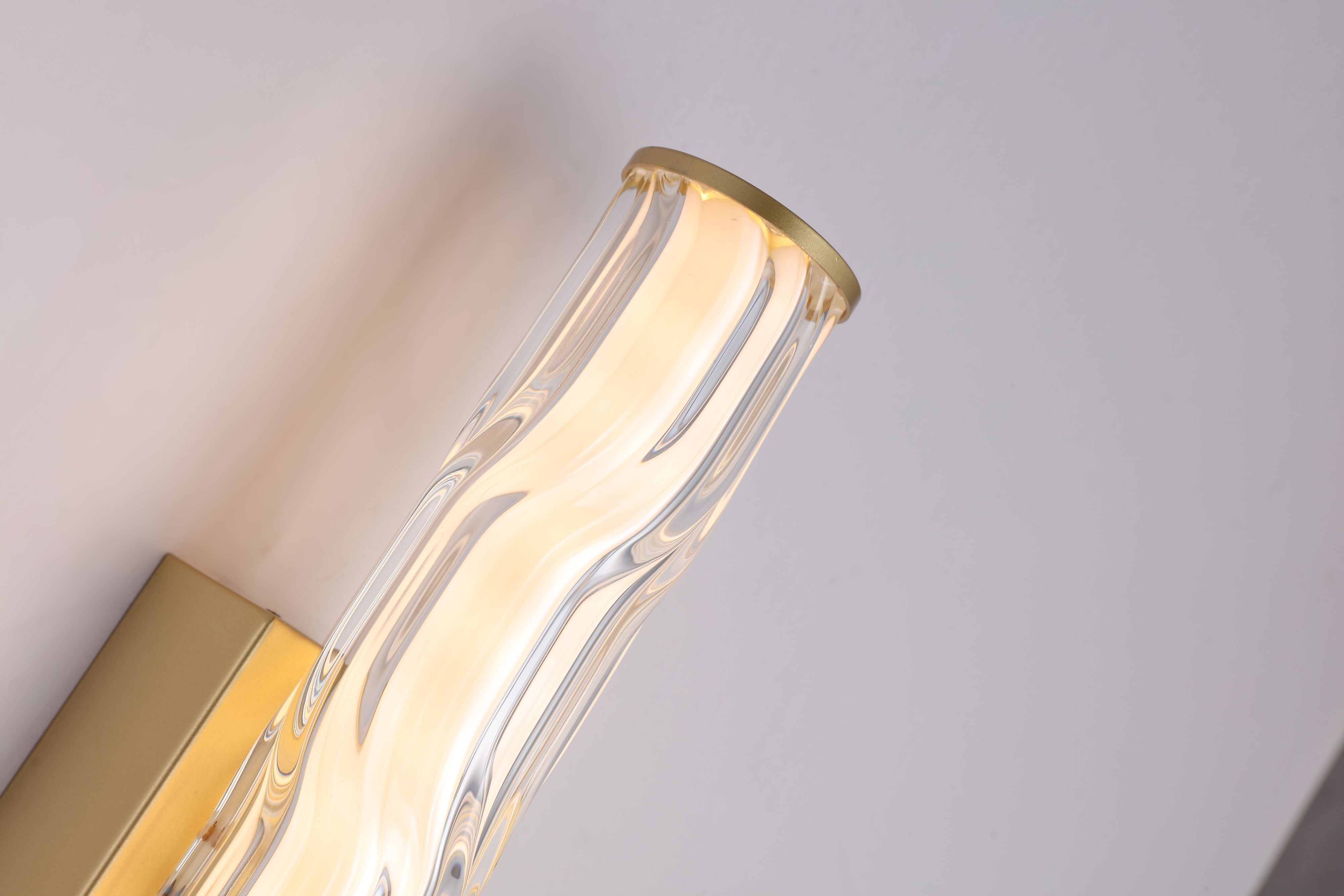 Close up of the Vibrate wall light's top end cap in matt gold, showing the wave ridged glass texture