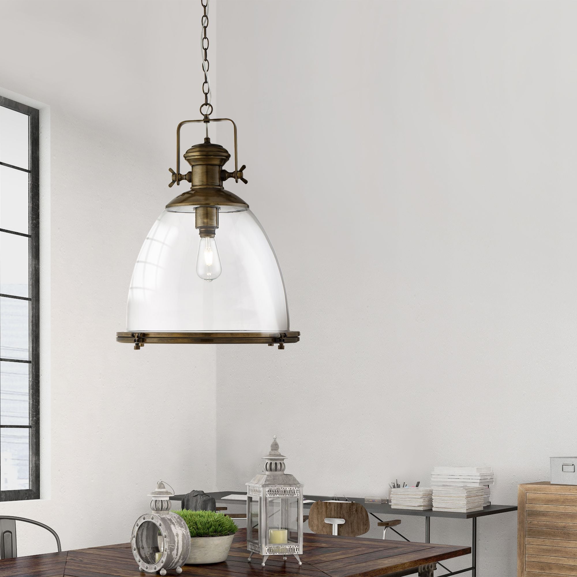 Searchlight Industrial pendant in antique brass and clear glass hung above a wooden dining table styled with lanterns and a potted plant