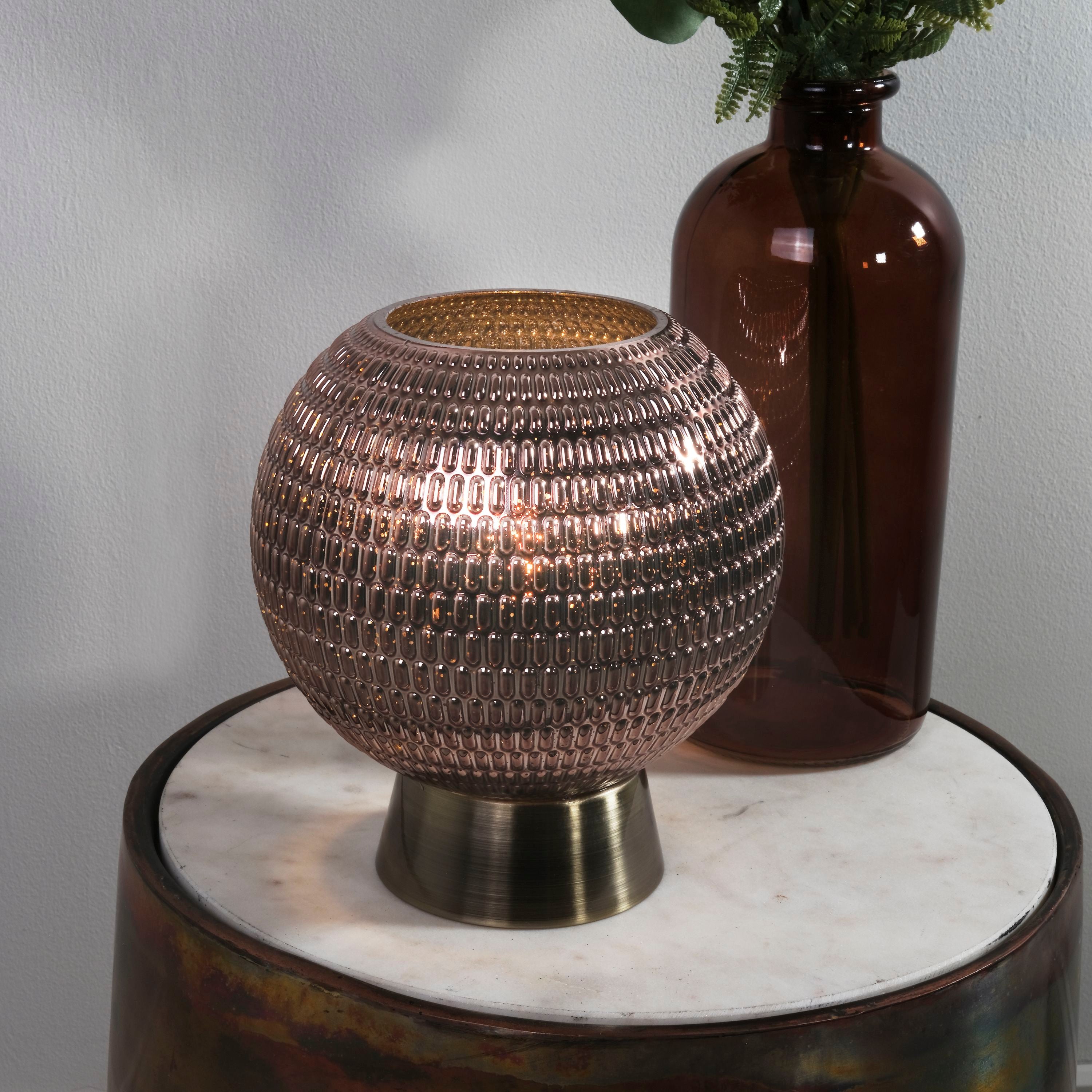 Searchlight Mila table lamp lit and styled on a table beside a brown glass bottle vase with green foliage