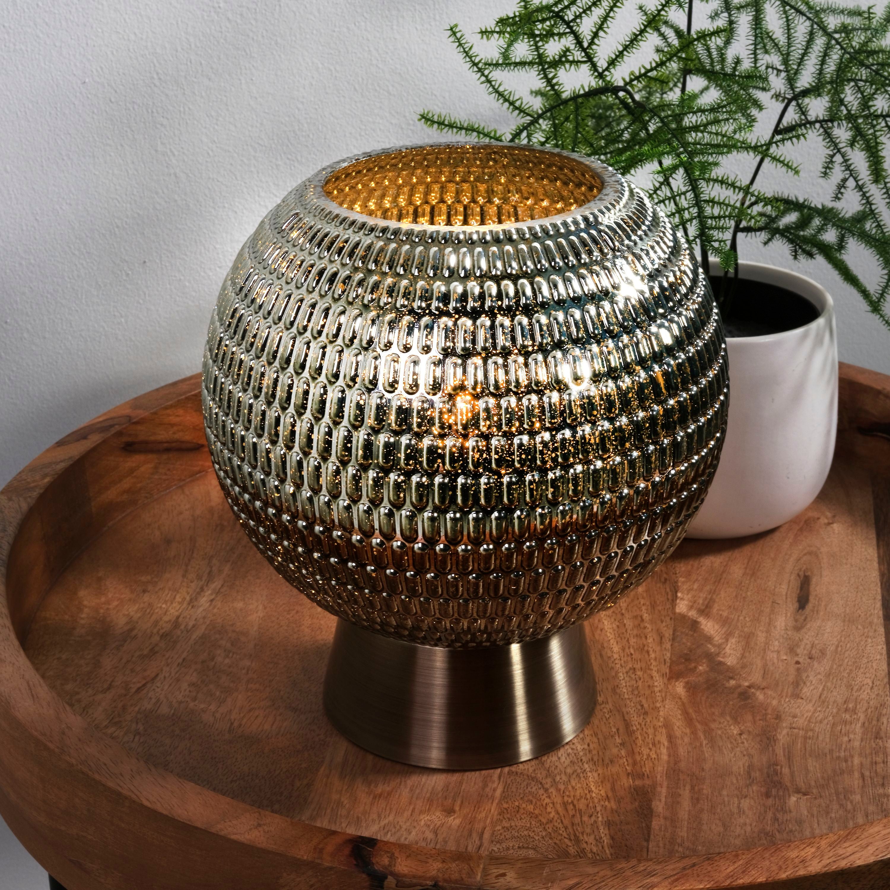 Mila table lamp styled on a round wooden side table next to a potted fern, lit with a warm glow in a home setting