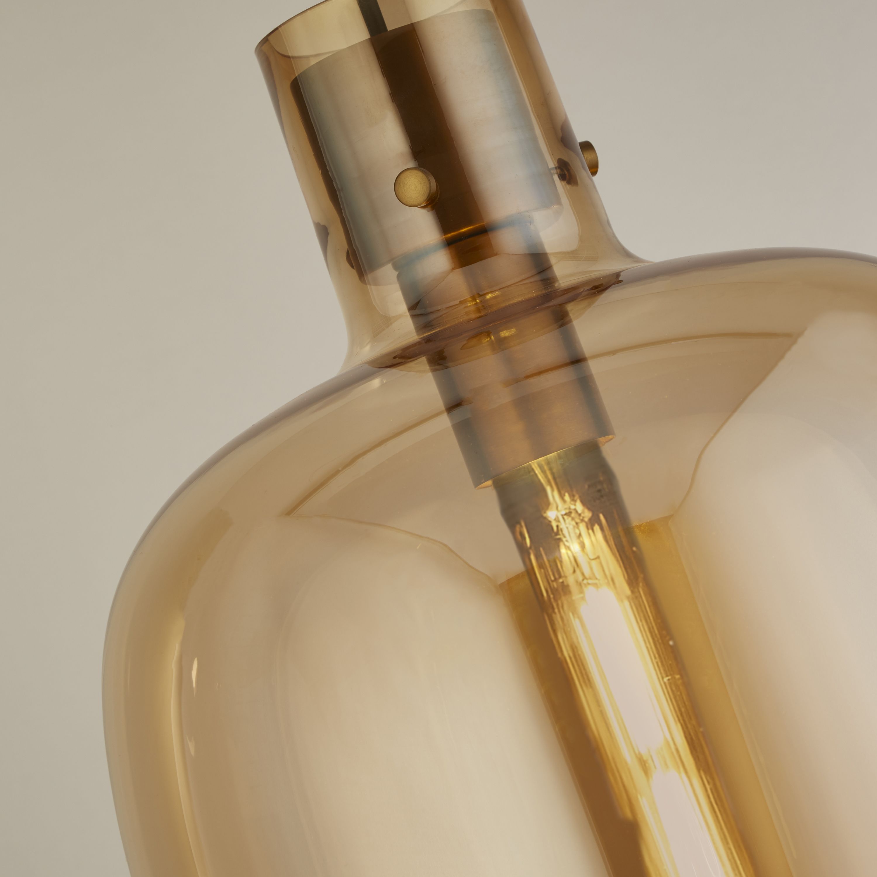 Close up of the satin brass fitting and amber glass shade on the Searchlight Barrel pendant, showing the lit bulb inside
