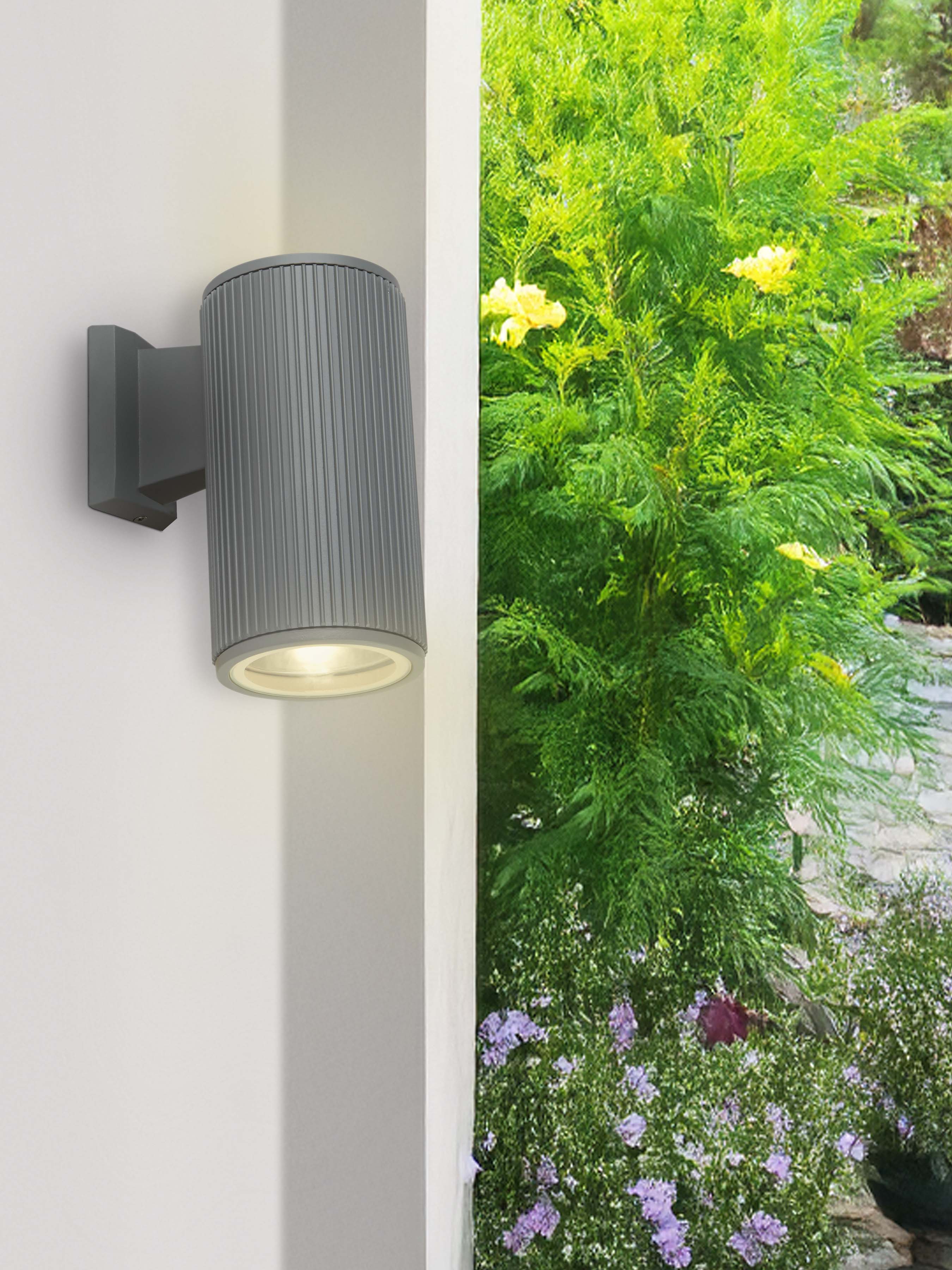 Hamburg Outdoor Wall Light installed on a white exterior wall corner at dusk, casting light down onto a green garden bed.