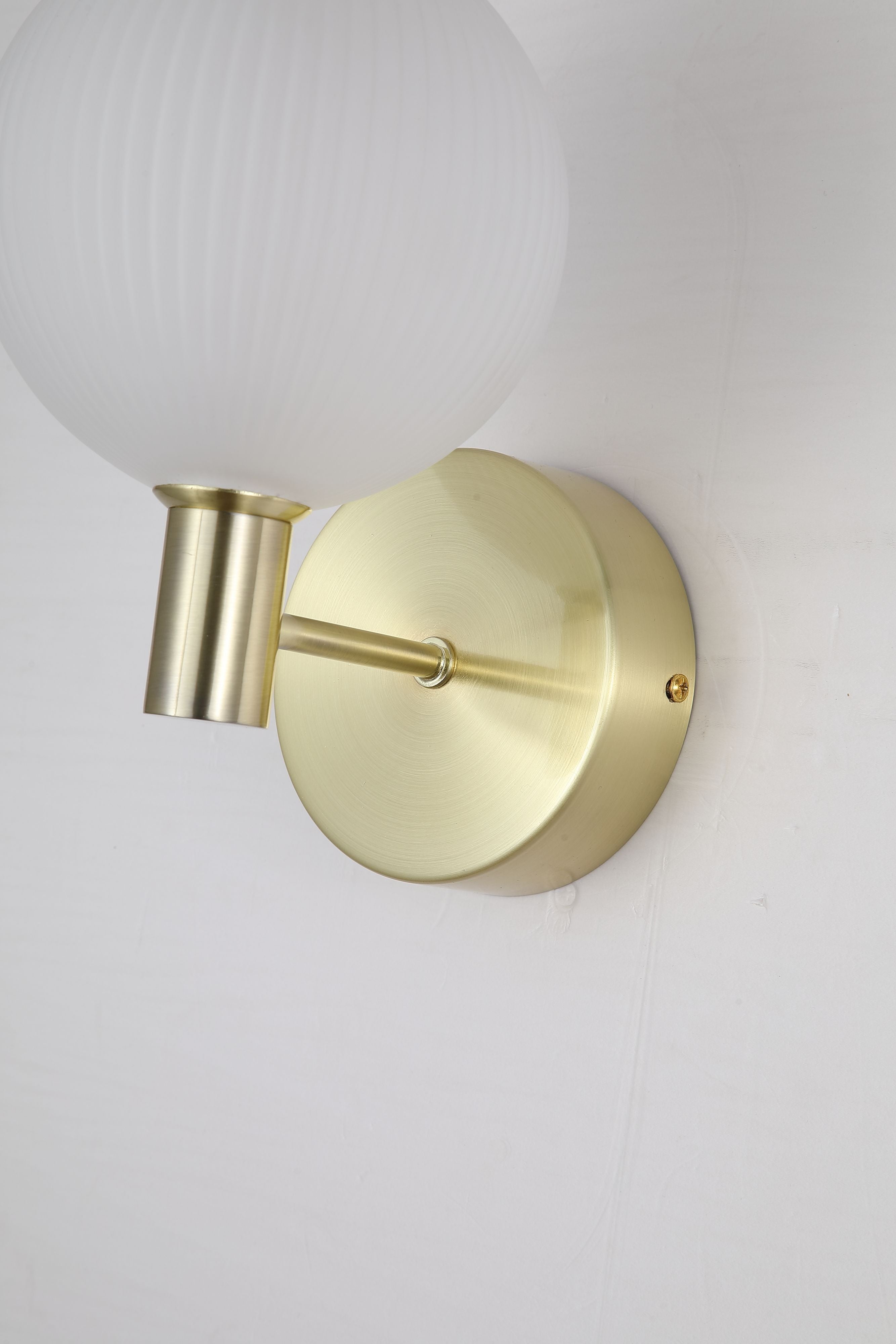 Close up angled view of the Searchlight Luminique LED Wall Light in satin brass, showing the circular backplate, arm and ribbed glass globe