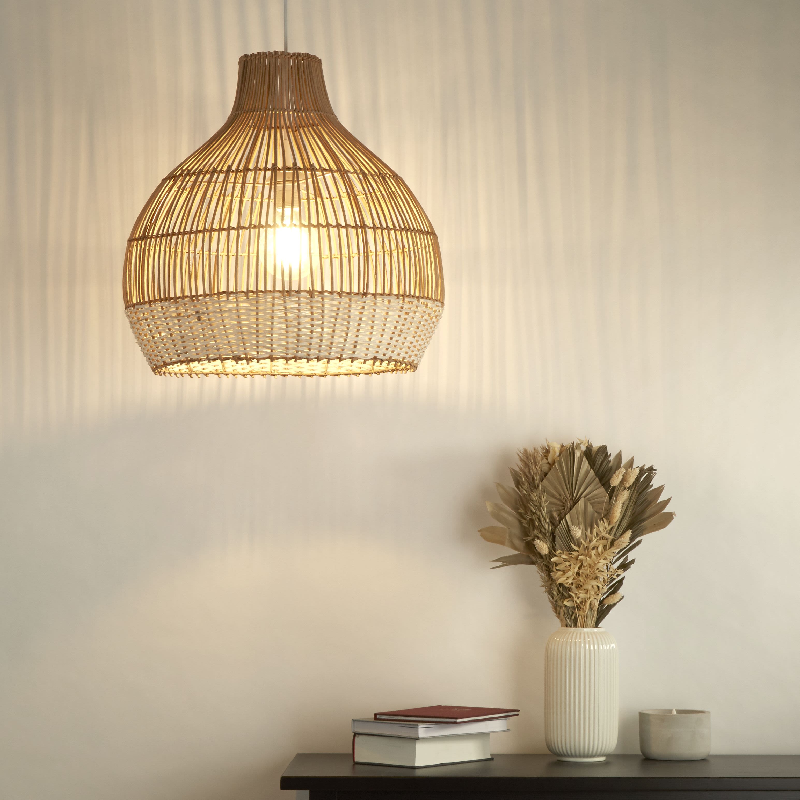 Searchlight Bali rattan pendant light styled in a room, hanging lit above a console table with dried flowers in a ceramic vase and a stack of books