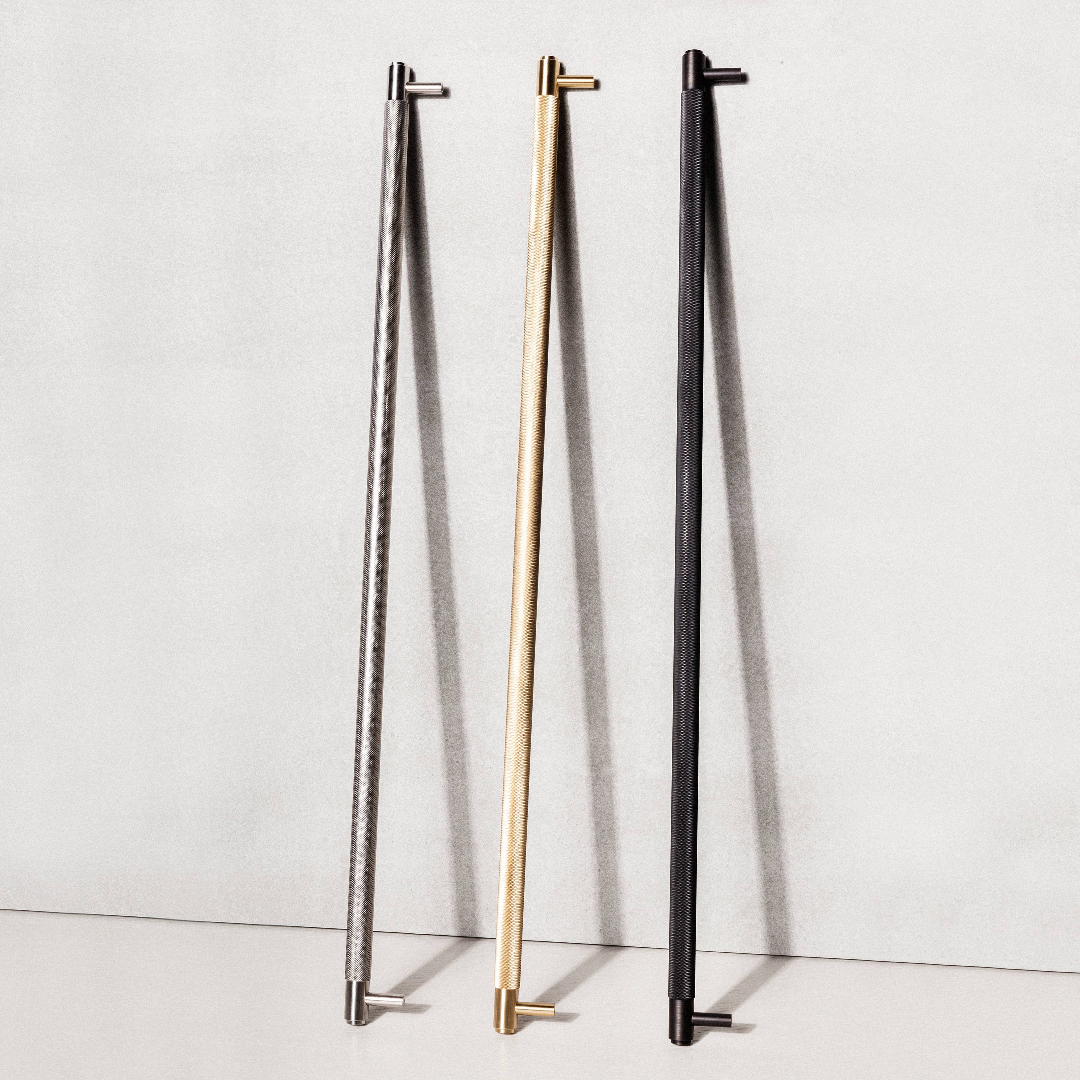 Closet bars shown in Steel, Brass and Black Cross Knurl finishes leaning against a wall