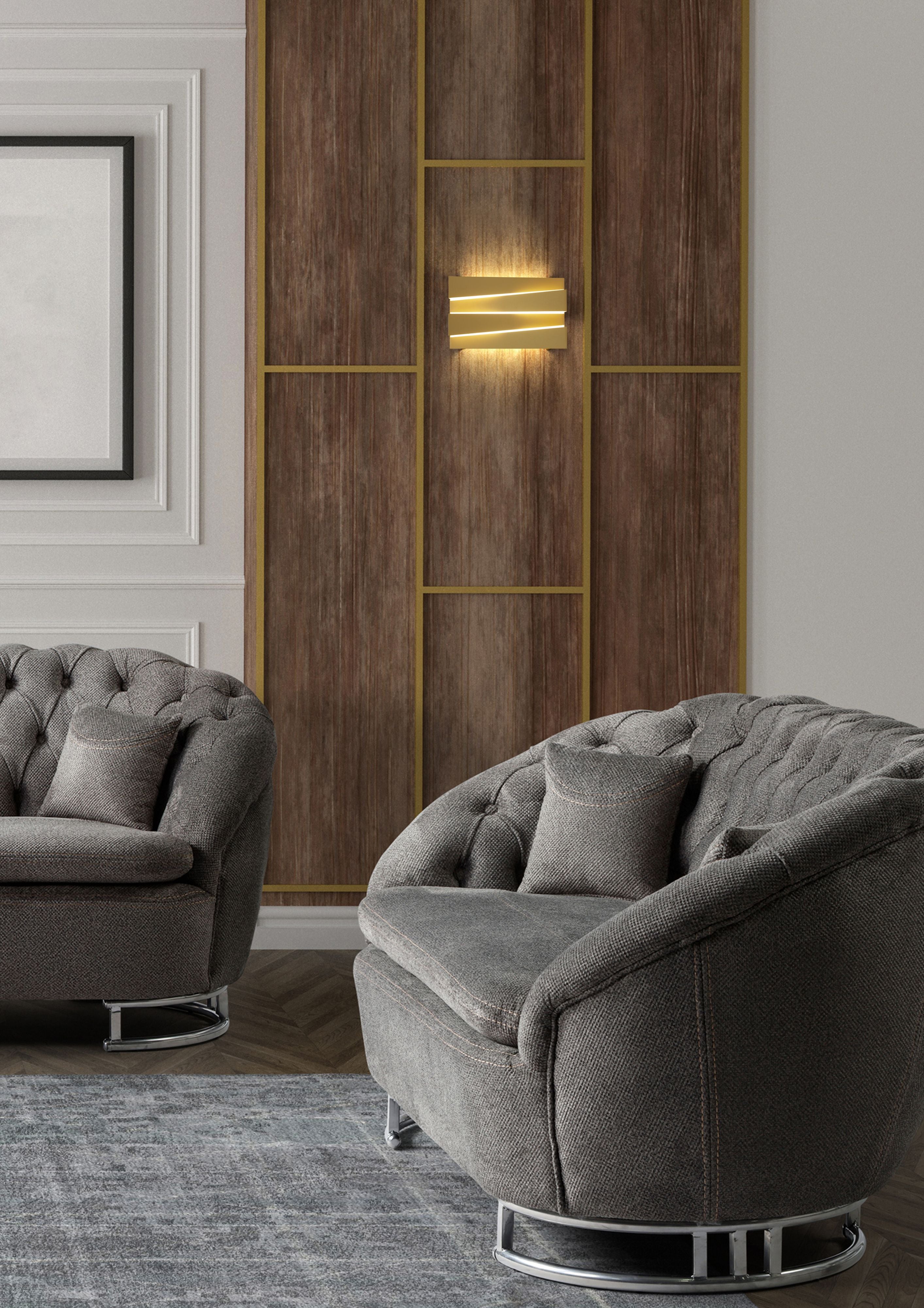 Wood panelled wall with brass trim, showing the Section wall light in sand gold lit and mounted between panels above two armchairs