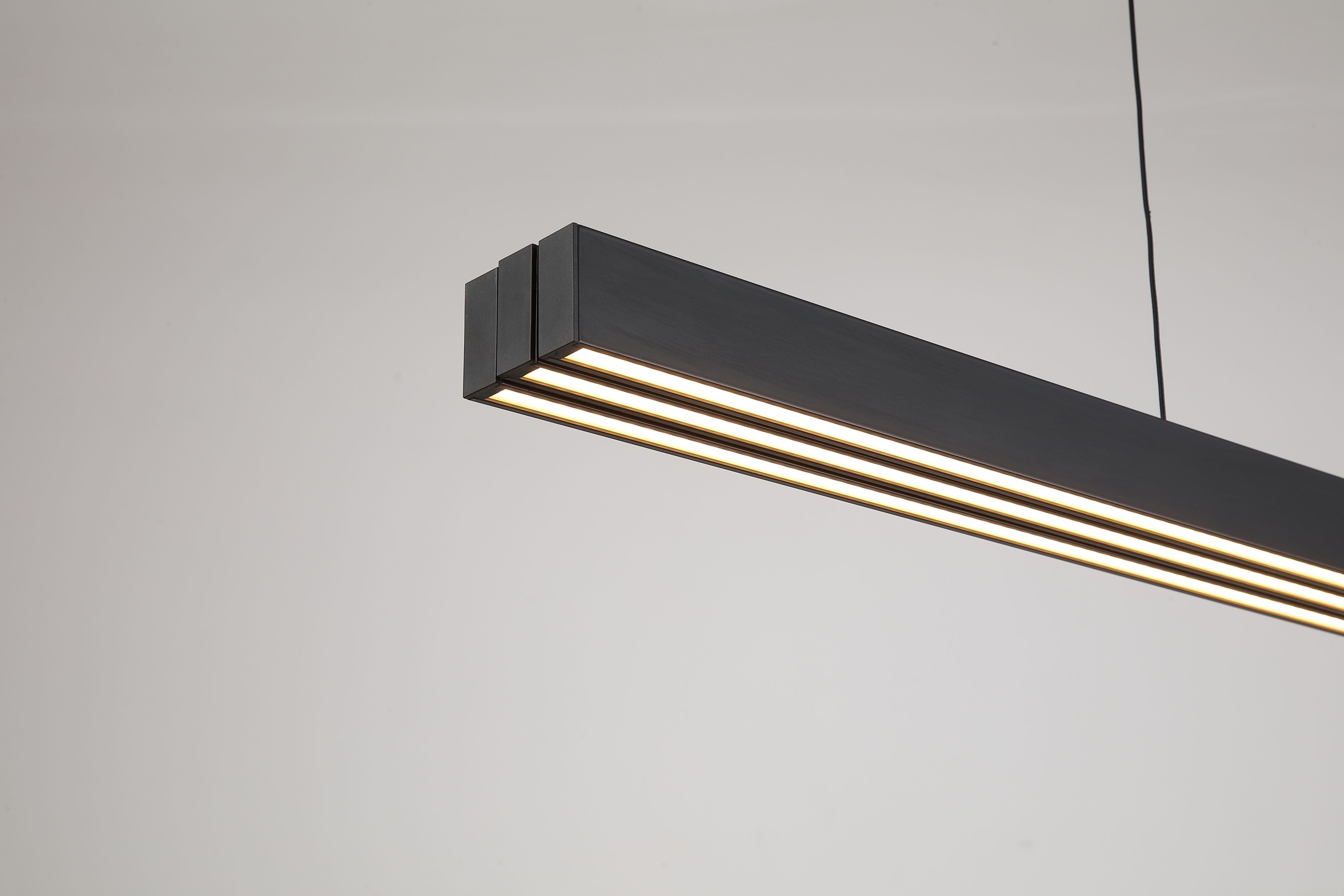 Close up of the Searchlight Linear LED pendant's matt black frame, showing the panel joins and the glowing frosted acrylic diffusers