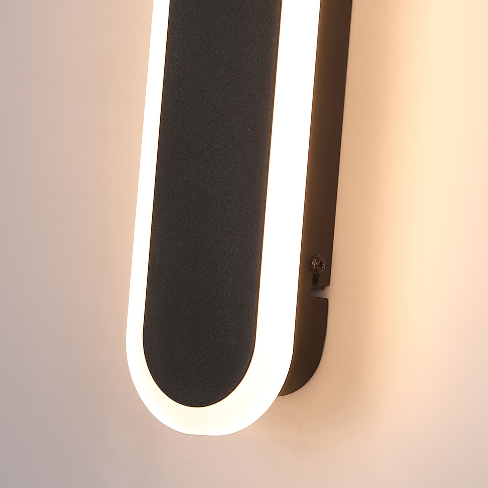 Close up of the rounded end of the Bordo 300mm wall light, lit, mounted on a wall showing the fixing screw