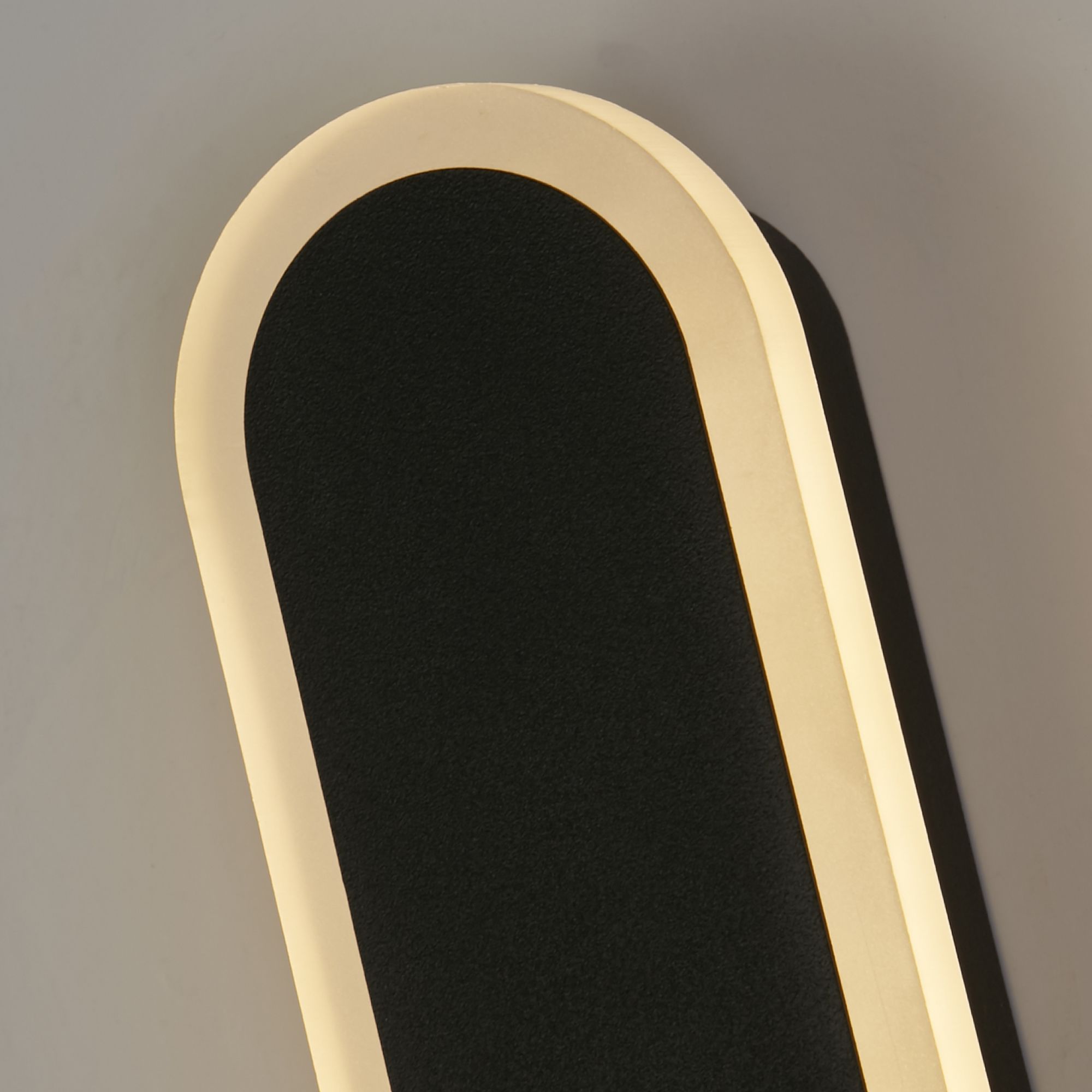 Close up of the rounded top end of the Bordo 600mm wall light, lit, mounted on a wall and casting a soft shadow