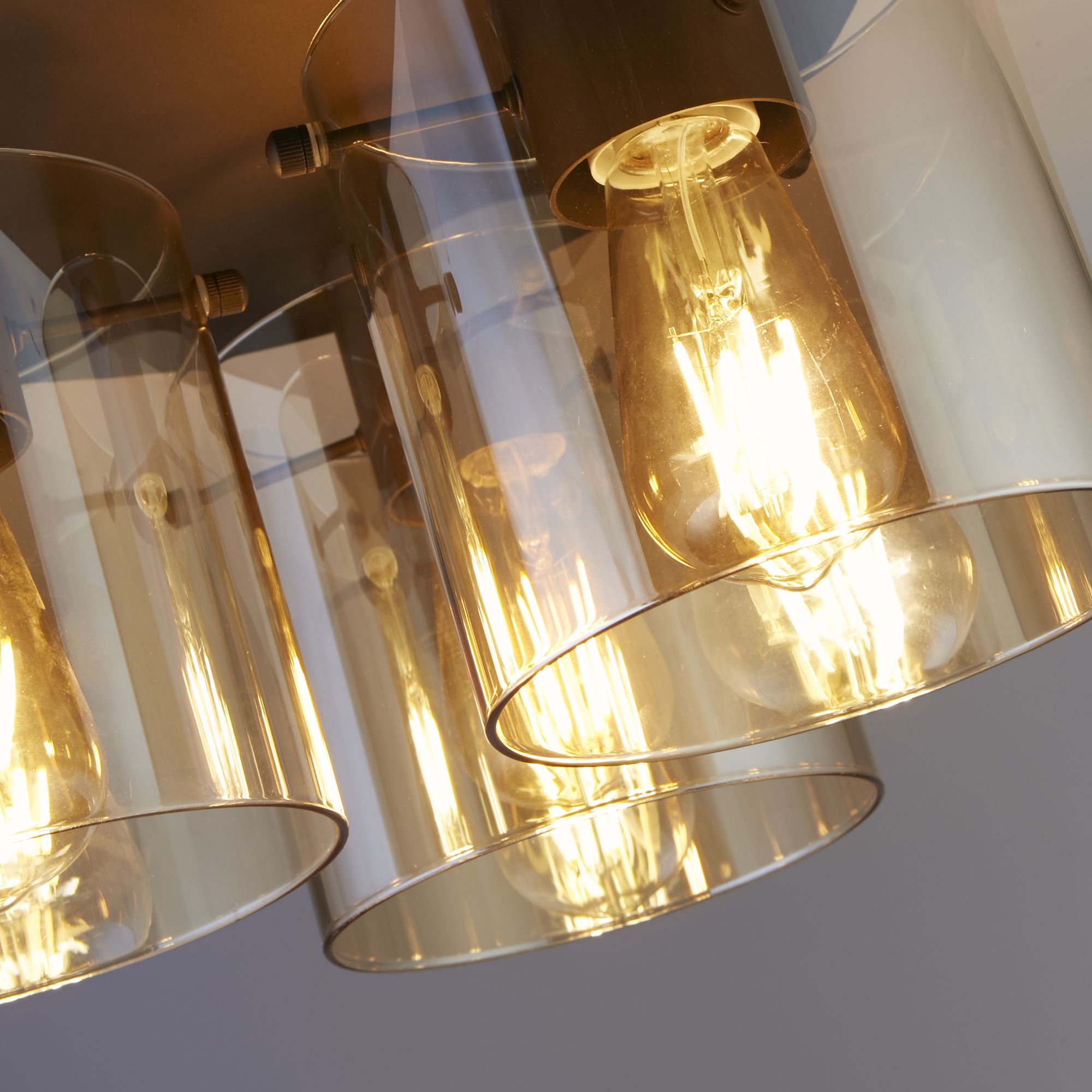 Close up angled view of the three amber glass shades and filament bulbs on the Searchlight Sweden 3 Light Flush