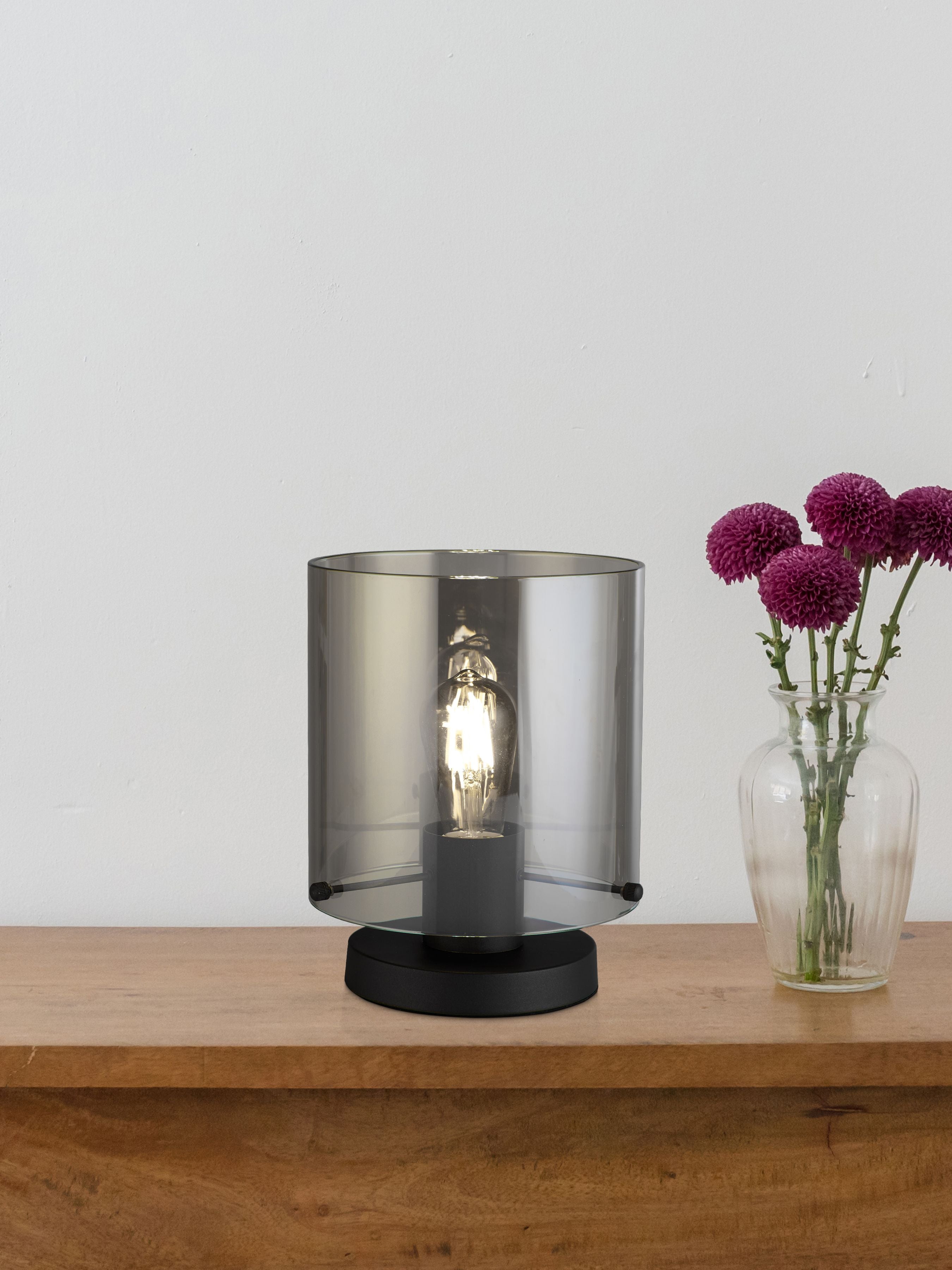 Searchlight Sweden 1 Light Table Lamp in matt black metal and smoked ombre glass styled on a wooden shelf beside a vase of purple flowers