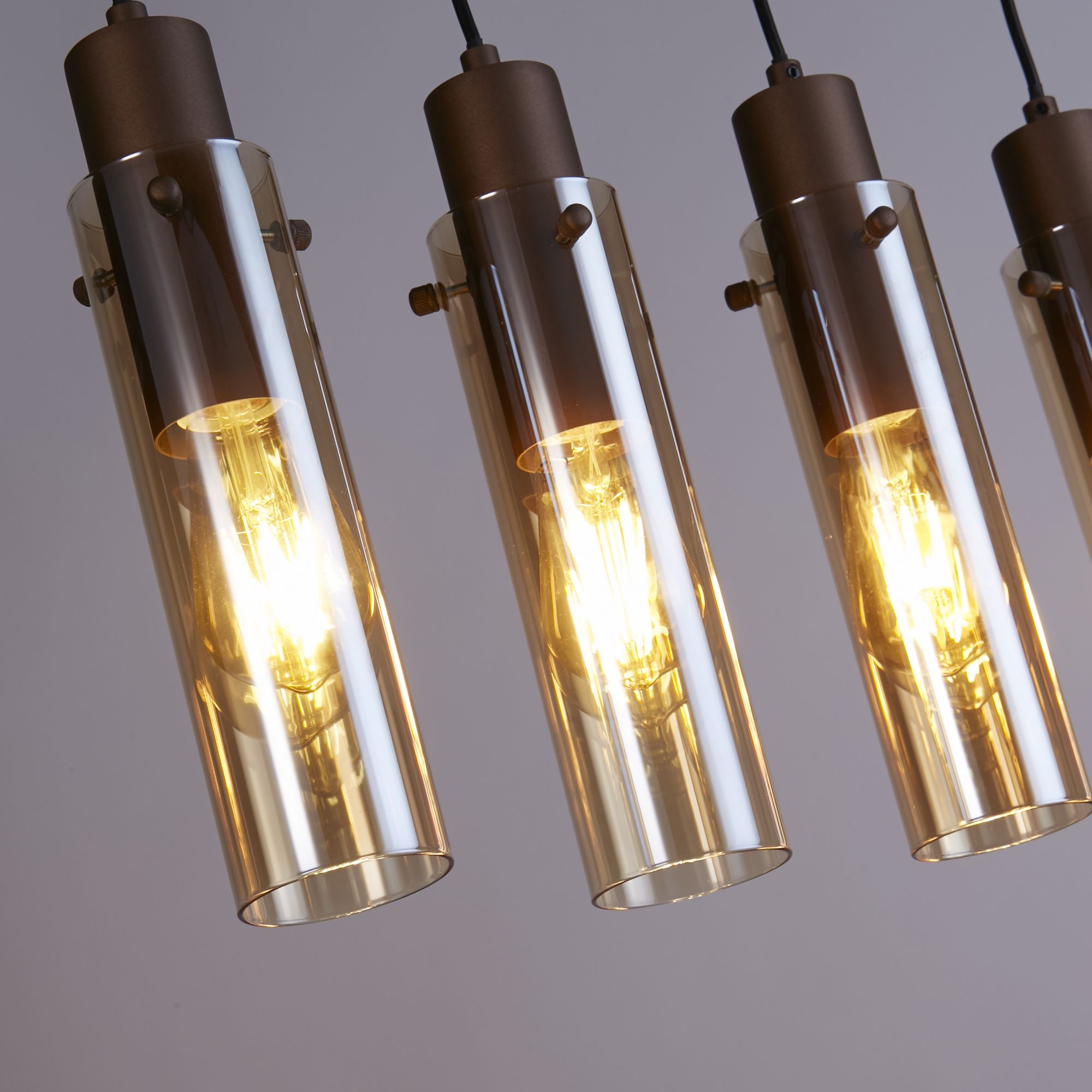 Close up of the amber glass tube shades and mocha metal fittings on the Sweden II 5 Light Bar Pendant, showing the fixing screws and lit bulbs